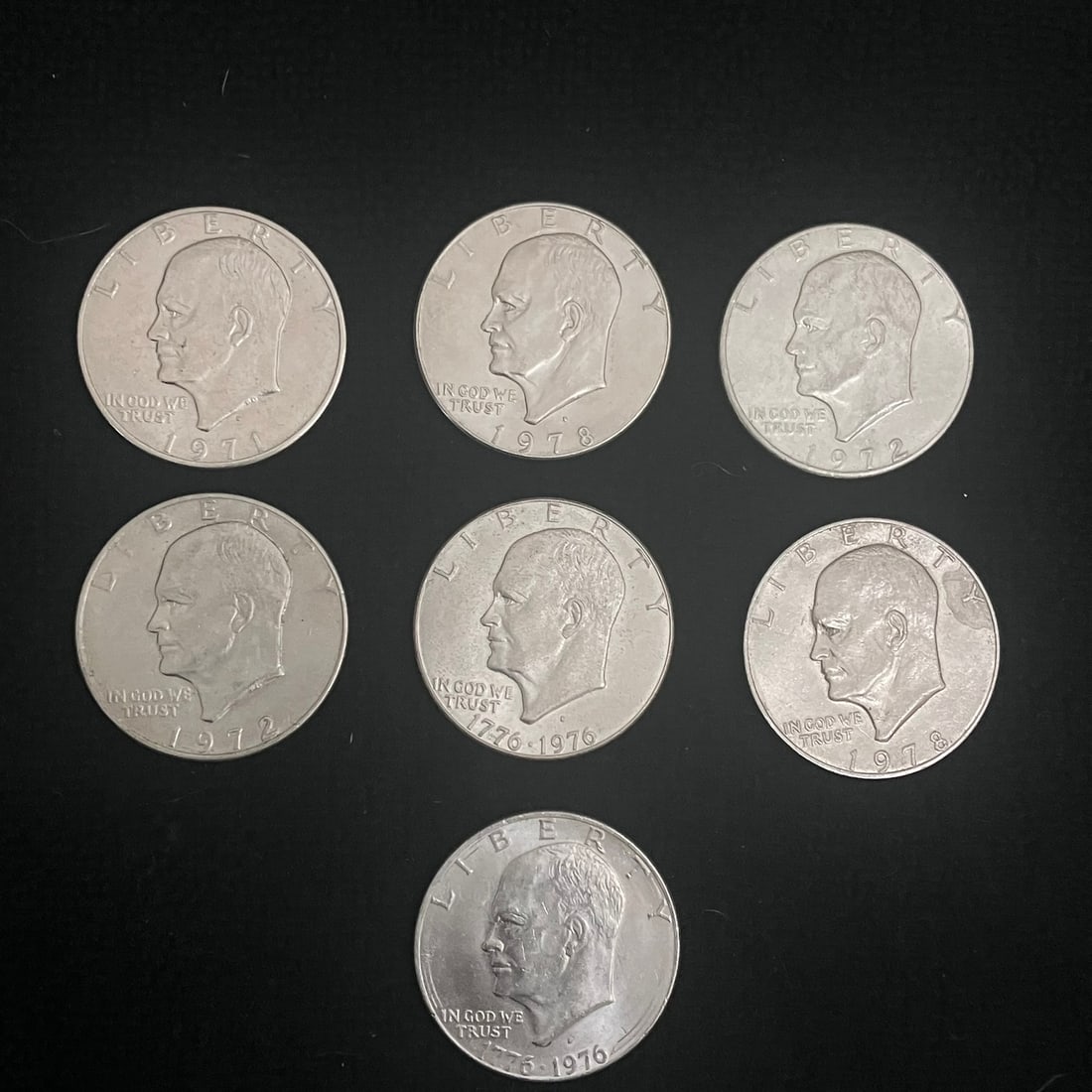 7 Eisenhower Dollar: Lot of seven United States one-dollar coins featuring the Eisenhower dollar design. Visible dates include 1971, 1972, 1978, and 1776-1976 bicentennial issues. Reverses shown include the standard eagle