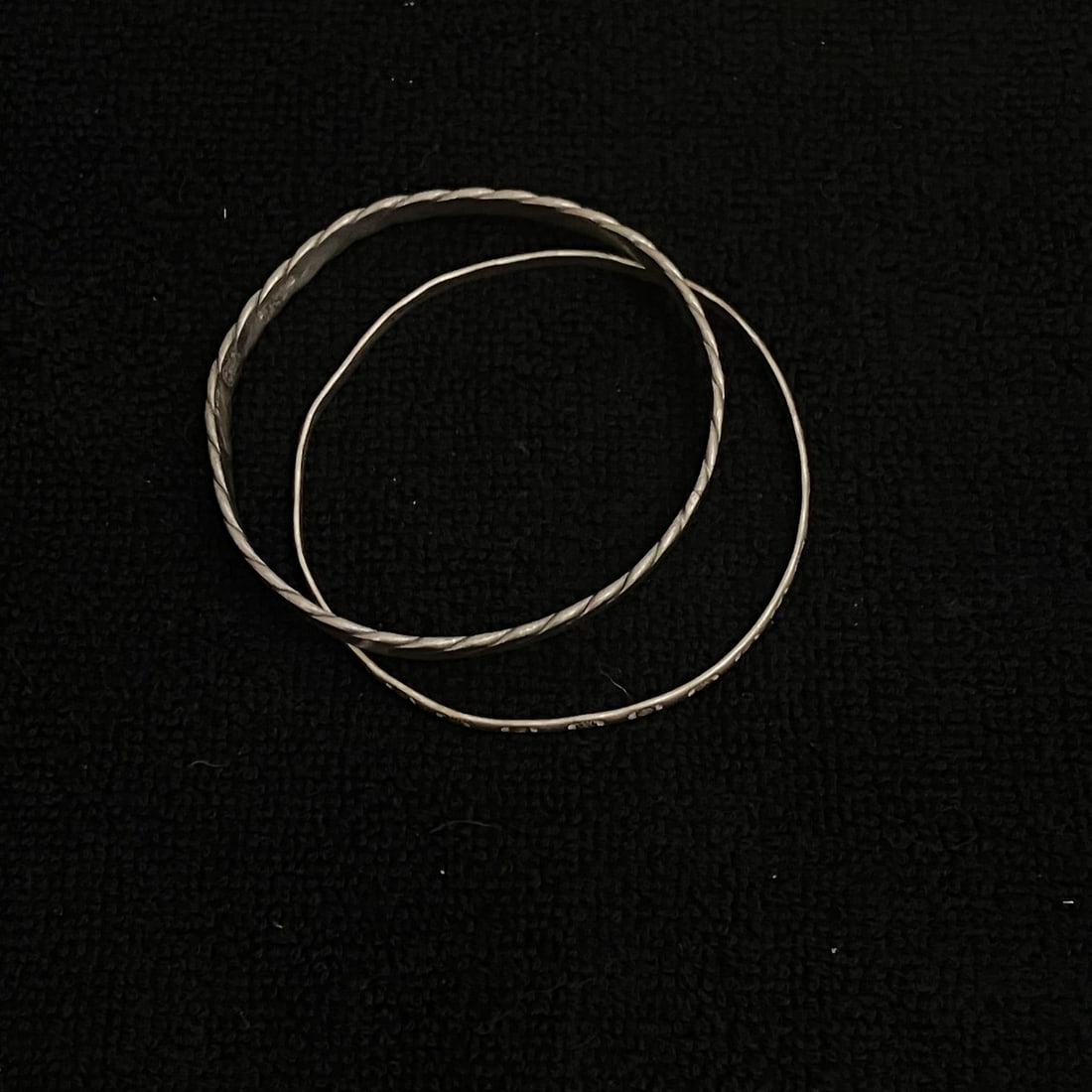 Pair of Sterling Silver Bangle 23.6 g: Pair of rigid silver-tone bangle bracelets. One bangle has a twisted band design and is stamped “STERLING 925” with an additional unresolved hallmark; the other has repeating stamped motifs