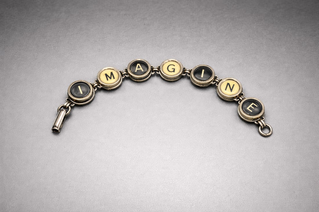Vintage Typewriter Key “IMAGINE” Bracelet: Vintage bracelet made from authentic typewriter keys spelling “IMAGINE.”Each round glass key is bezel-set in a silver-tone metal frame and linked with articulated connectors. Mixed black and c