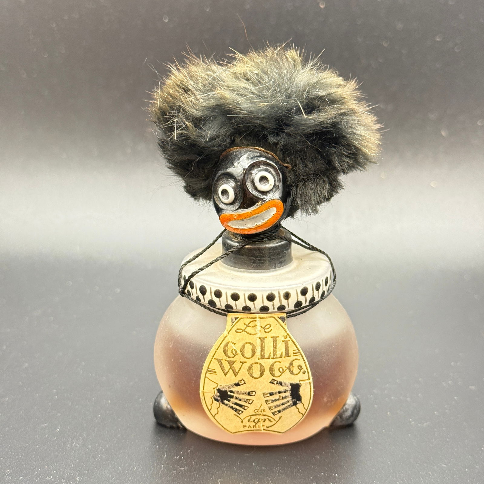 1930's DeVigny Golliwog Perfume Bottle: Bottle by DeVigny, a whimsical perfume bottle based on the literary character Golliwog created by Florence Kate Upton. Light wear from age, still has some perfume in the bottle. Label intact.