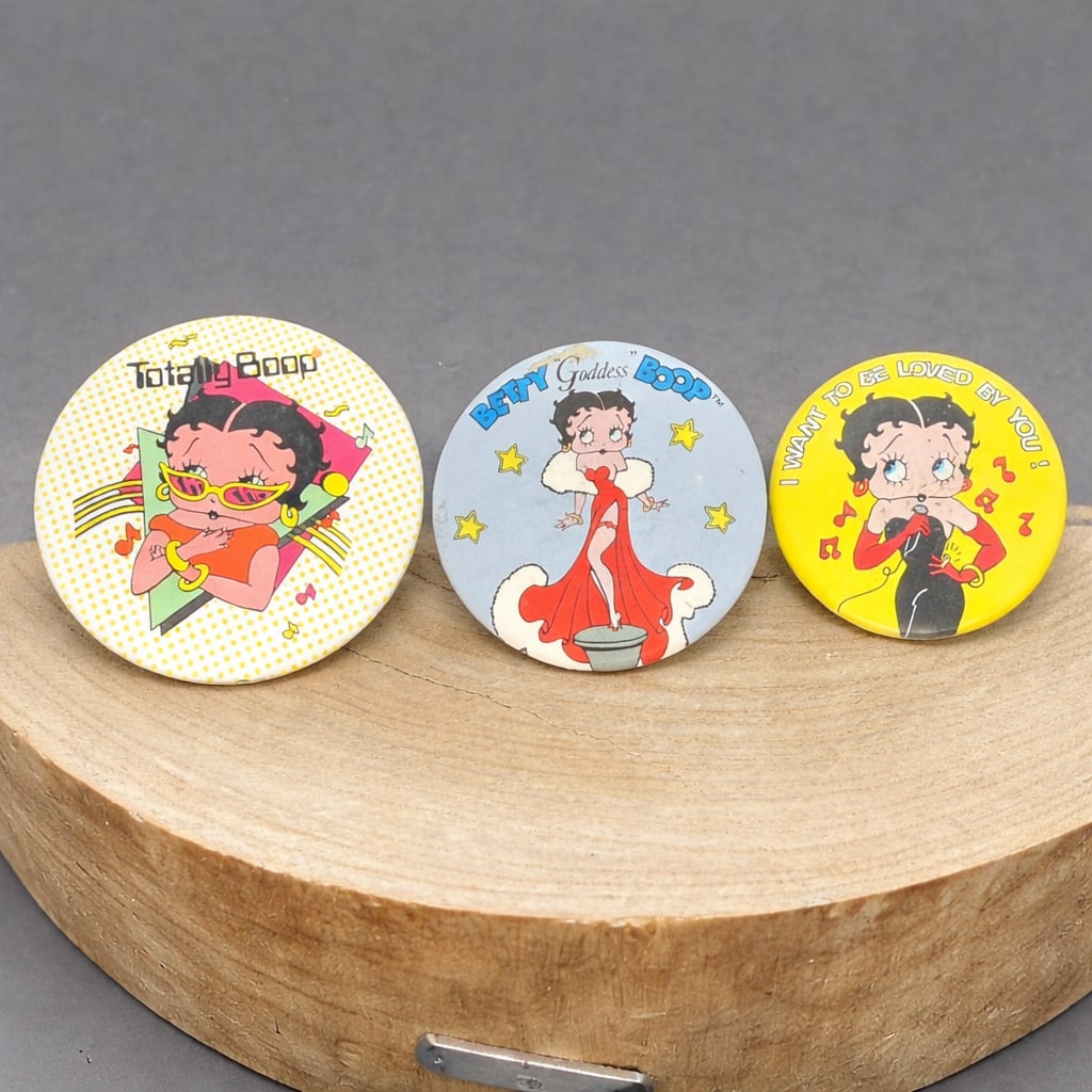 Three Vintage Betty Boop Pinback Buttons: Group of three vintage Betty Boop pinback buttons. Includes three different graphic designs: “Totally Boop,” “Betty Goddess Boop,” and “I Want to Be Loved by You.” Each feature