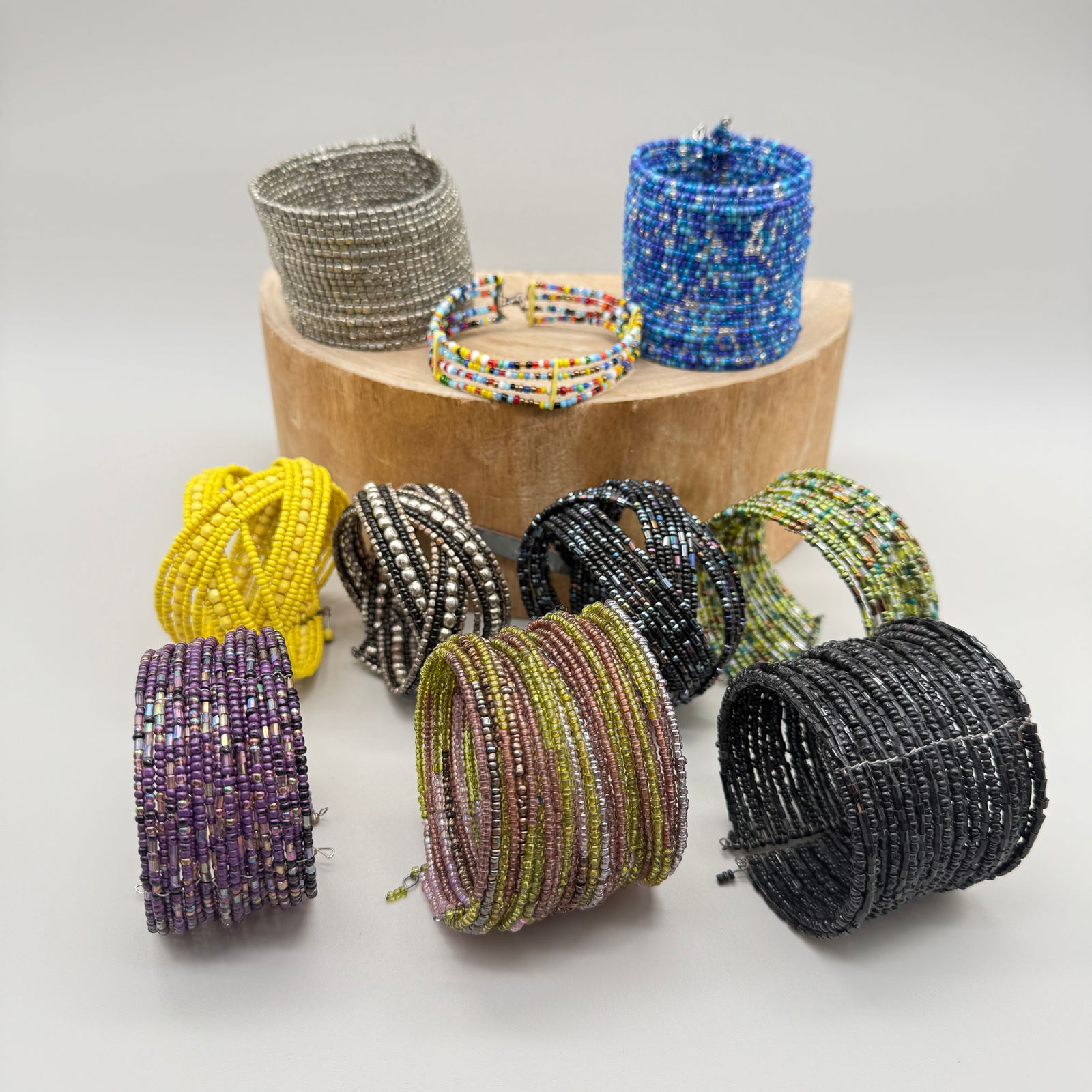 Lot of Ten Colorful Seed Bead Cuff Bracelets: Collection of ten seed bead cuff bracelets in a variety of vibrant and metallic colors, including blues, silvers, yellows, purples, greens, black, and multicolor patterns. Each cuff is constructed of