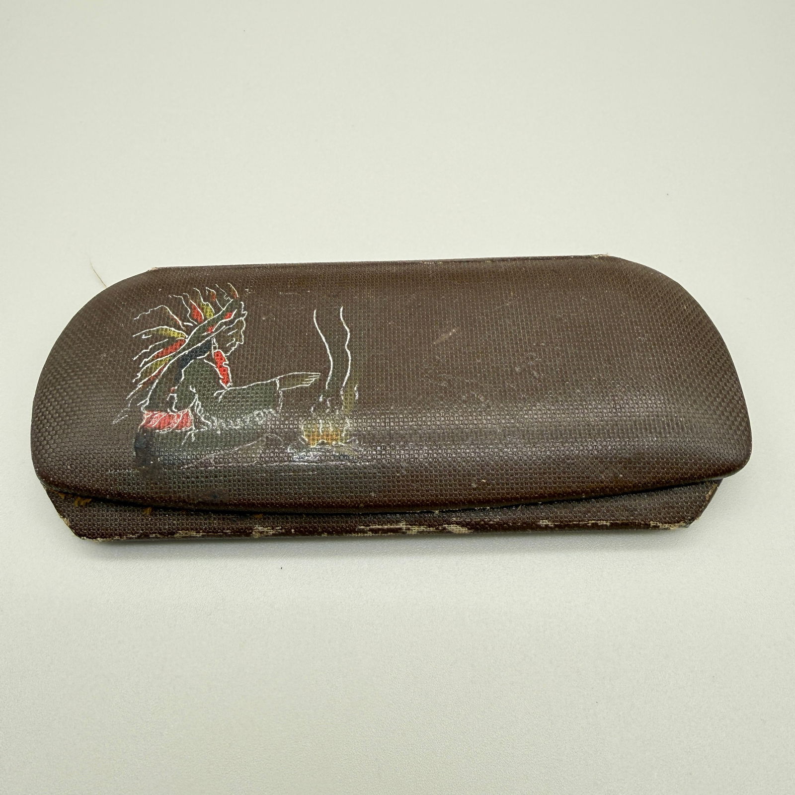 Hand Painted Native American Vintage Eyeglass Case: Vintage hard eyeglass case featuring a hand-painted Native American motif with campfire scene on textured brown exterior. Interior has fabric peeling. Exterior also shows age-related wear including sc