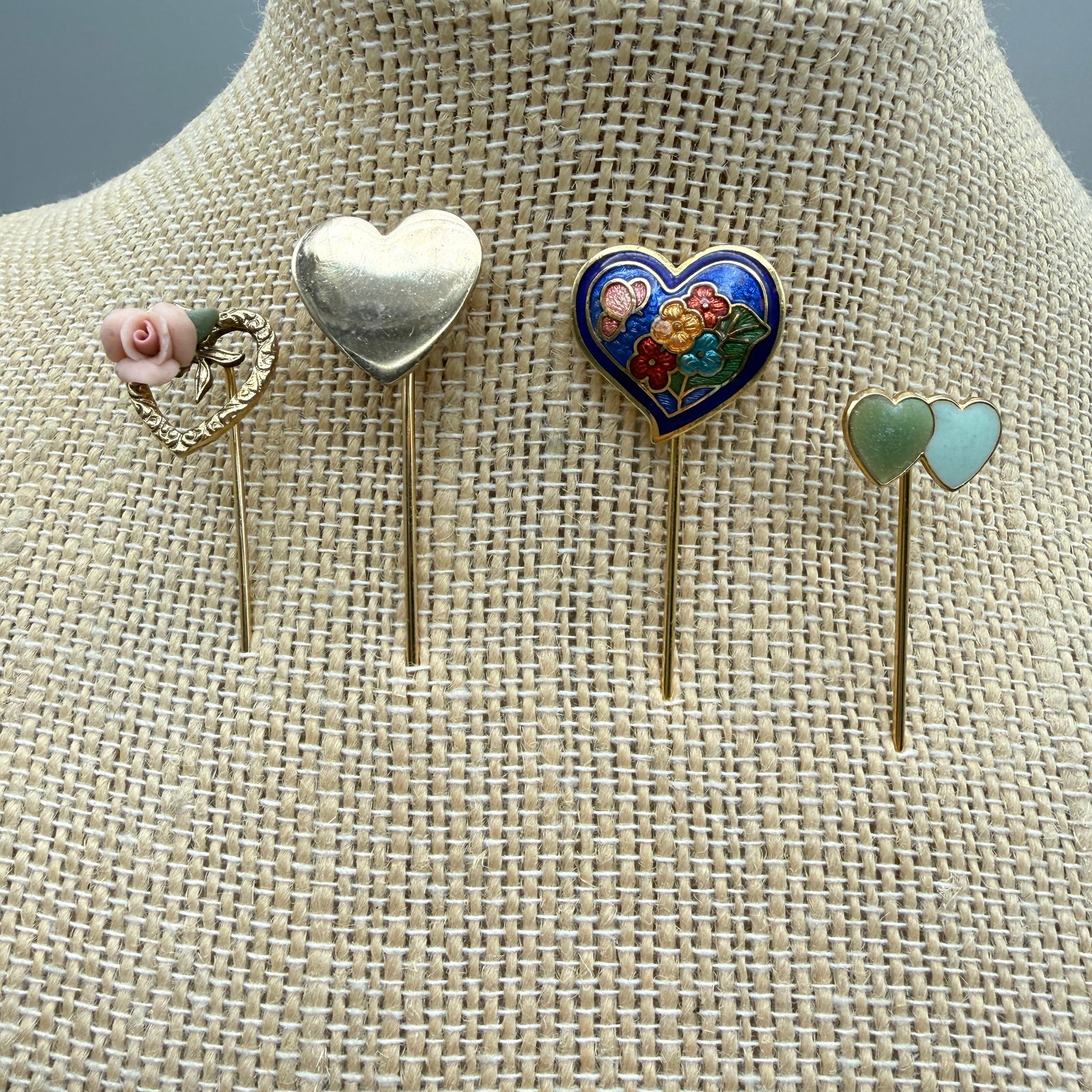 Vintage Heart Stick Pins Group: Group of four vintage stick pins featuring heart motifs. Designs include a cloisonné enamel heart with floral decoration, polished metal hearts, a double heart with green stone inlay, and a decorativ