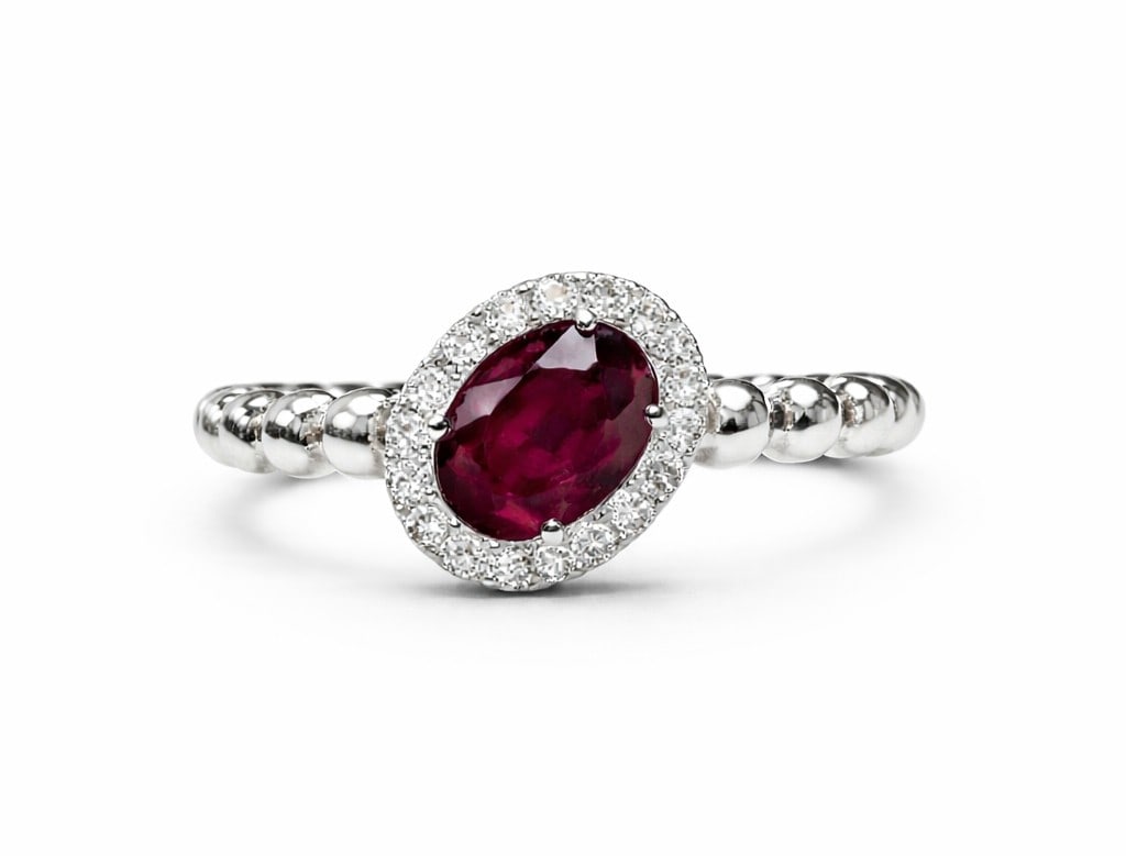 0.69ct Oval Ruby and 0.15ctw Diamond Slanted Halo 14K White Gold Ring: An exquisite masterpiece of haute joaillerie, this magnificent Slanted Halo ring featuring Ruby, Diamond is a true treasure. A detailed Halo gallery secures the stones, rendered in 2.14 grams of lustr