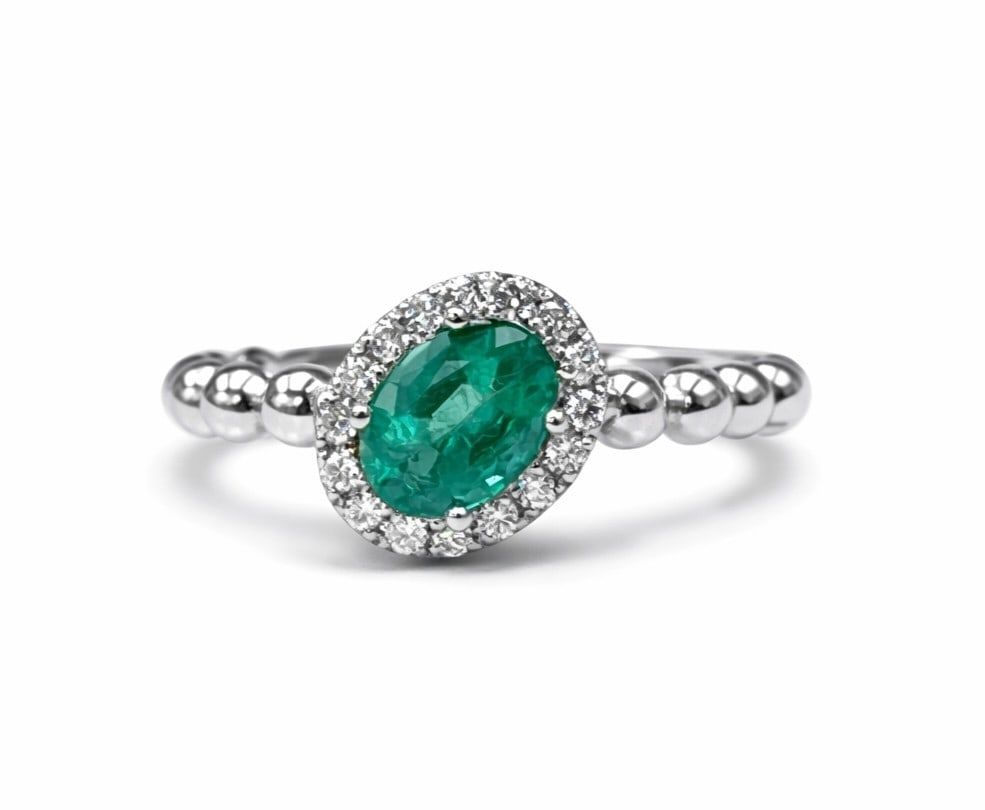 0.77ct Oval Emerald and 0.14ctw Diamond 14K White Gold Ring: Captured in a moment of brilliance, this magnificent Slanted Ring featuring Emerald and White Diamond speaks to the connoisseur. The gemstones are nestled within a Halo framework, supported by a subst
