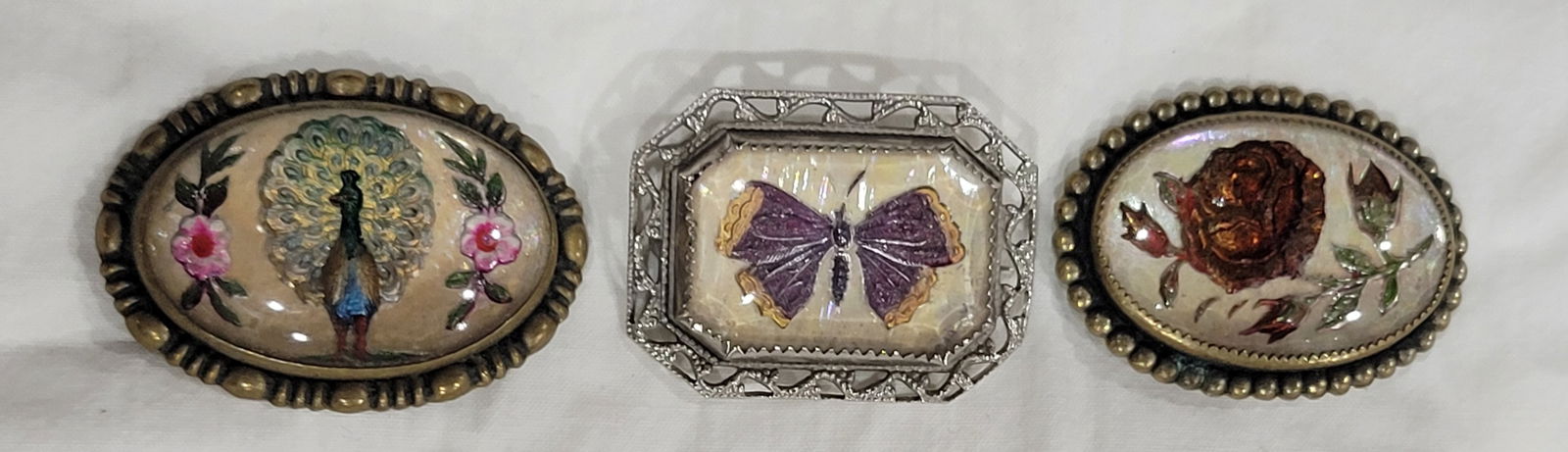 Set of Three Bubble Glass Brooches: Antique Goofus Glass Brooch Pin with detailed Peacock with tail fanned out featured with Pink Flowers and cream colored background, Antique Goofus Glass Brooch Pin with decorative Purple and Gold Butt