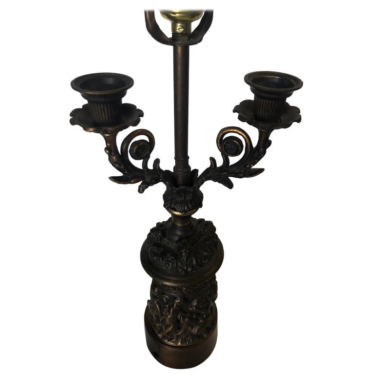 Neo-Classic Bronze Patina Cherub Candelabra Table Lamp: Neo-Classic Bronze Cherub Candelabra Table Lamp featuring a single light socket and Two Candleholders. The table lamp features a heavy relief of Cherubs wrapping around the base and scrolling patterns
