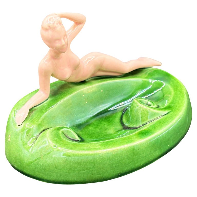 Mid-century Pink & Green Nude Lounging Female Ceramic Ashtray Ceramic Ashtray: Mid-century Era pink and green Nude Female ceramic ashtray. The ashtray features a beautifully abstract pink nude female figure on a green, organic-shaped ashtray. It comes in a gloss finish that high
