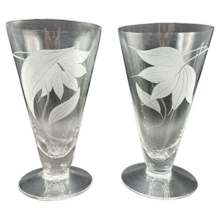 Mid-century Dorothy Thorpe Style Footed Tumbler w/ Etched Tropical Lilies, Pair: Attributed to the style of Dorothy Thorpe, this pair of footed tumblers feature an elegant etched design of exotic tropical lilies and botanical motifs. Both glasses feature Thorpe's iconic minimalism