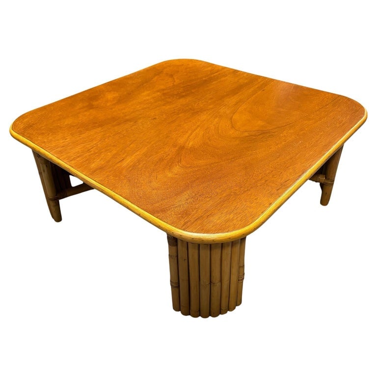 Restored 3' Sqaure Rattan Coffee Table w/ Vertically Stacked Legs: This beautifully restored Paul Frankl-inspired oversized 37" square coffee table with 8-strand vertically stacked rattan legs and a mahogany wood top with a rattan trim along the borders. Underneath t