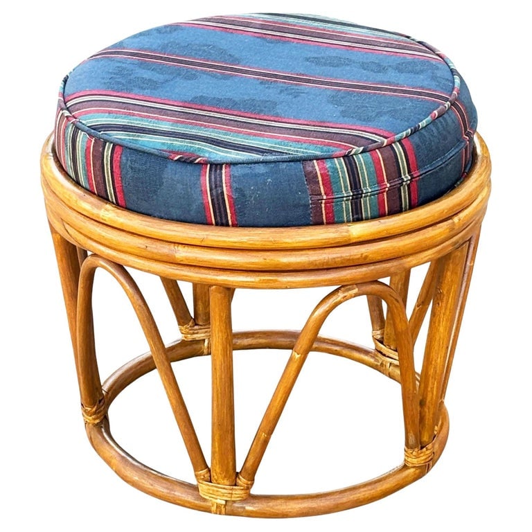 Restored Rattan Footstool with Striped Jacquard Navy Cushion: Vintage rattan stool featuring a circular bentwood frame with natural honey patina and arched supports for added strength and style. The seat cushion is upholstered in a vibrant blue jacquard fabric w