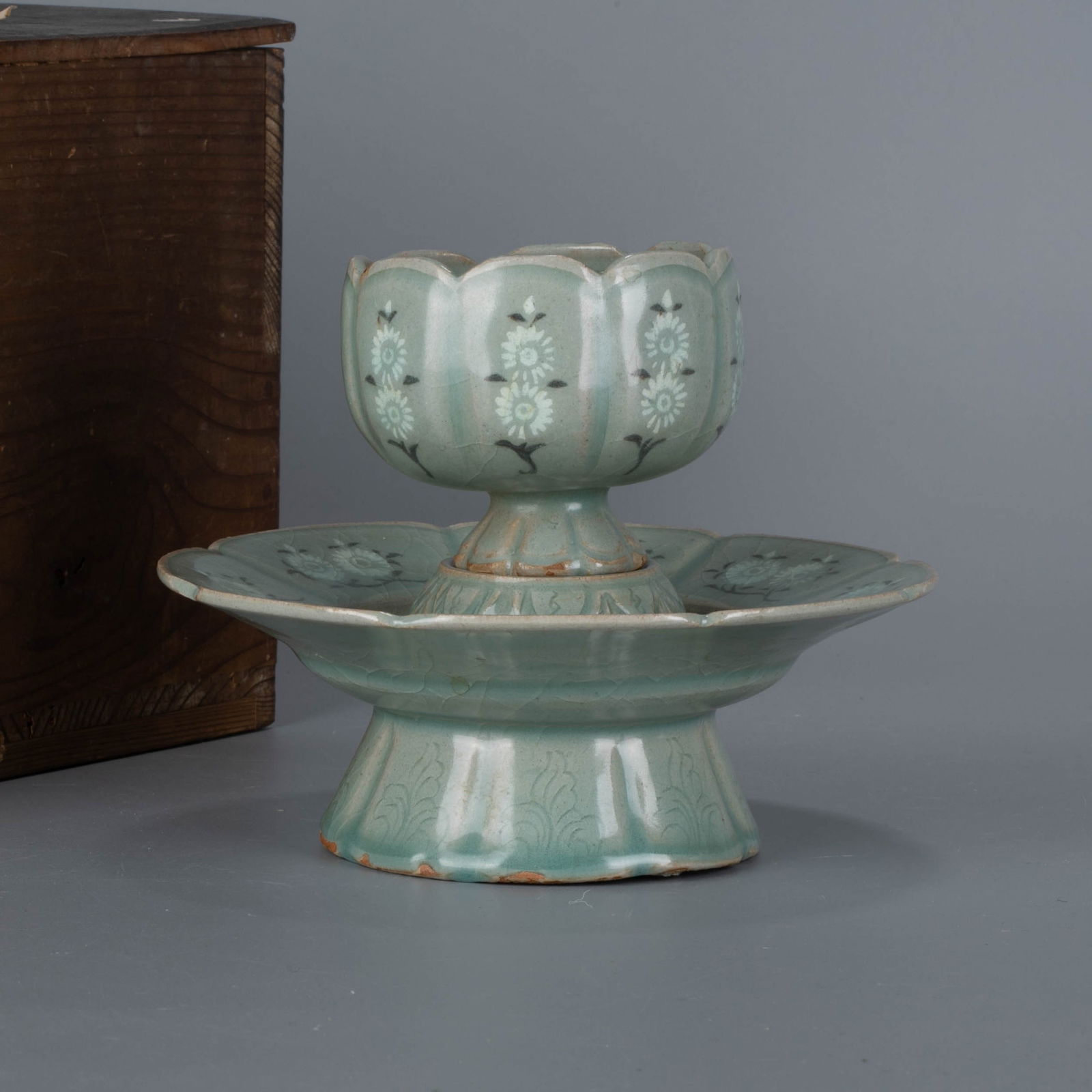 Goryeo black and white elephant inlaidtea bowl stand: The tea Bowl stand is in the lobed rim style, with a flap at the top and a high base at the bottom. the whole body is covered with green glaze, and the glaze color is soft and bluish. the plate mouth