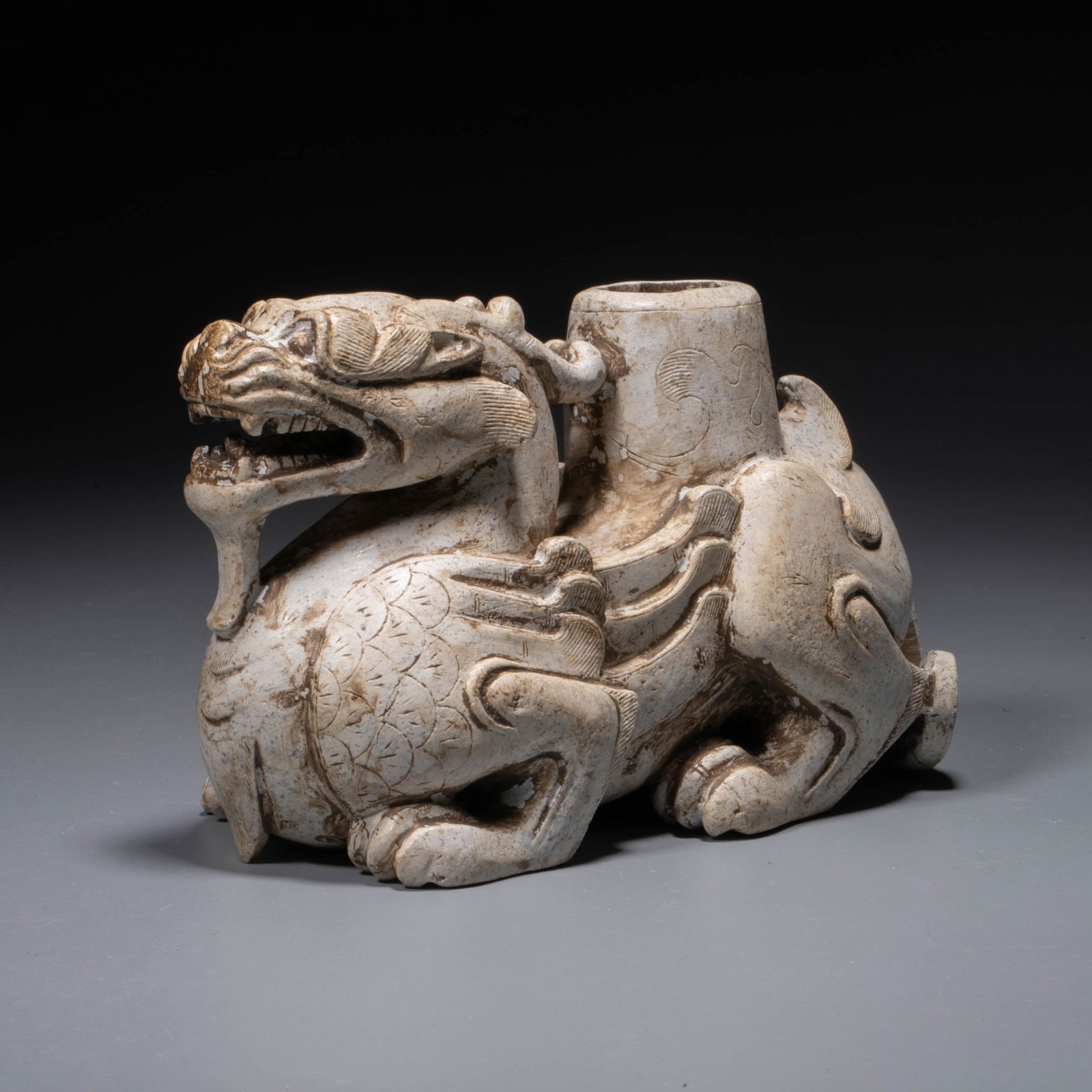 Han Jade to ward off evil spirits: Carved in the round, the mythical bixie is depicted in a recumbent pose, raising its head with mouth agape and fangs exposed, its round eyes wide open in a fierce expression. The wings extend closely