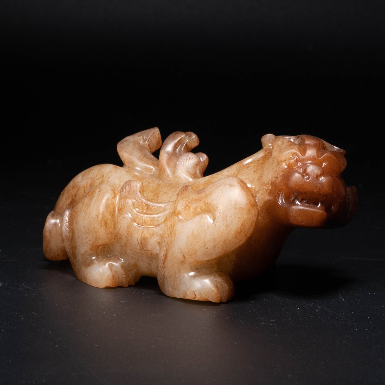 Han Dynasty white jade red auspicious beast: This auspicious white jade and red beast from the Han Dynasty is in the shape of a prostrate and crouching figure, with its head held high, its mouth open and its teeth exposed, with a majestic and