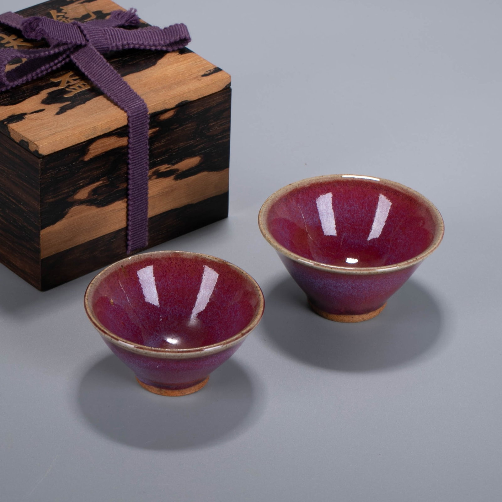 Qing Dynasty kiln-transformed red-glazed pair of cups, in a shared black persimmon wood box with: Qing Dynasty kiln-transformed red-glazed pair of cups, in a shared black persimmon wood box with gold-lacquered inscription