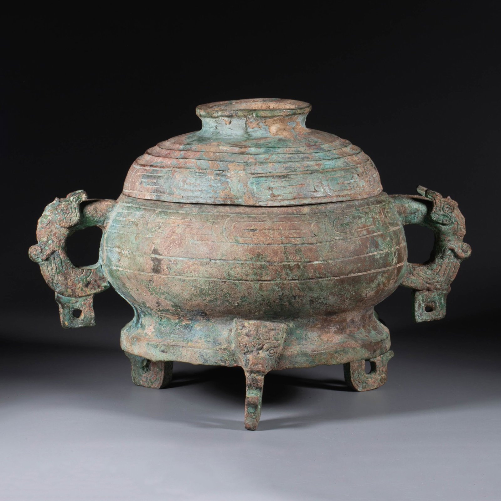 Western Zhou gui ritual food vessel: This piece is Western Zhou style with a lid, with a rounded mouth and bulging belly, a round handle on the top, a ring base with three animal heads and small feet, dragon heads on both sides holding