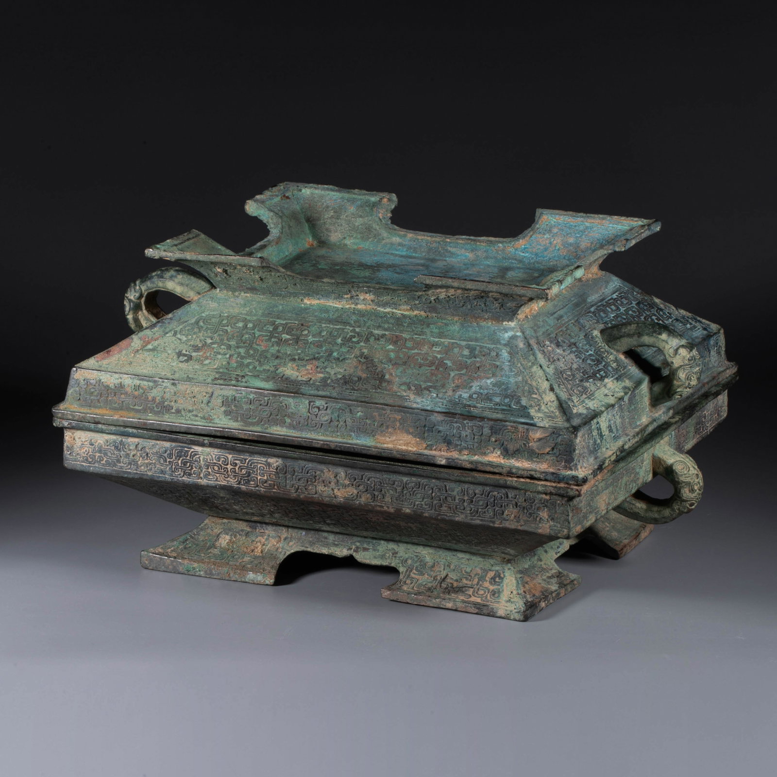 Spring and Autumn Period: This bronze fu is of the rectangular, box-shaped form, with a matching cover designed to fit symmetrically over the vessel. It features a wide everted rim with a square lip, sloping sides that taper