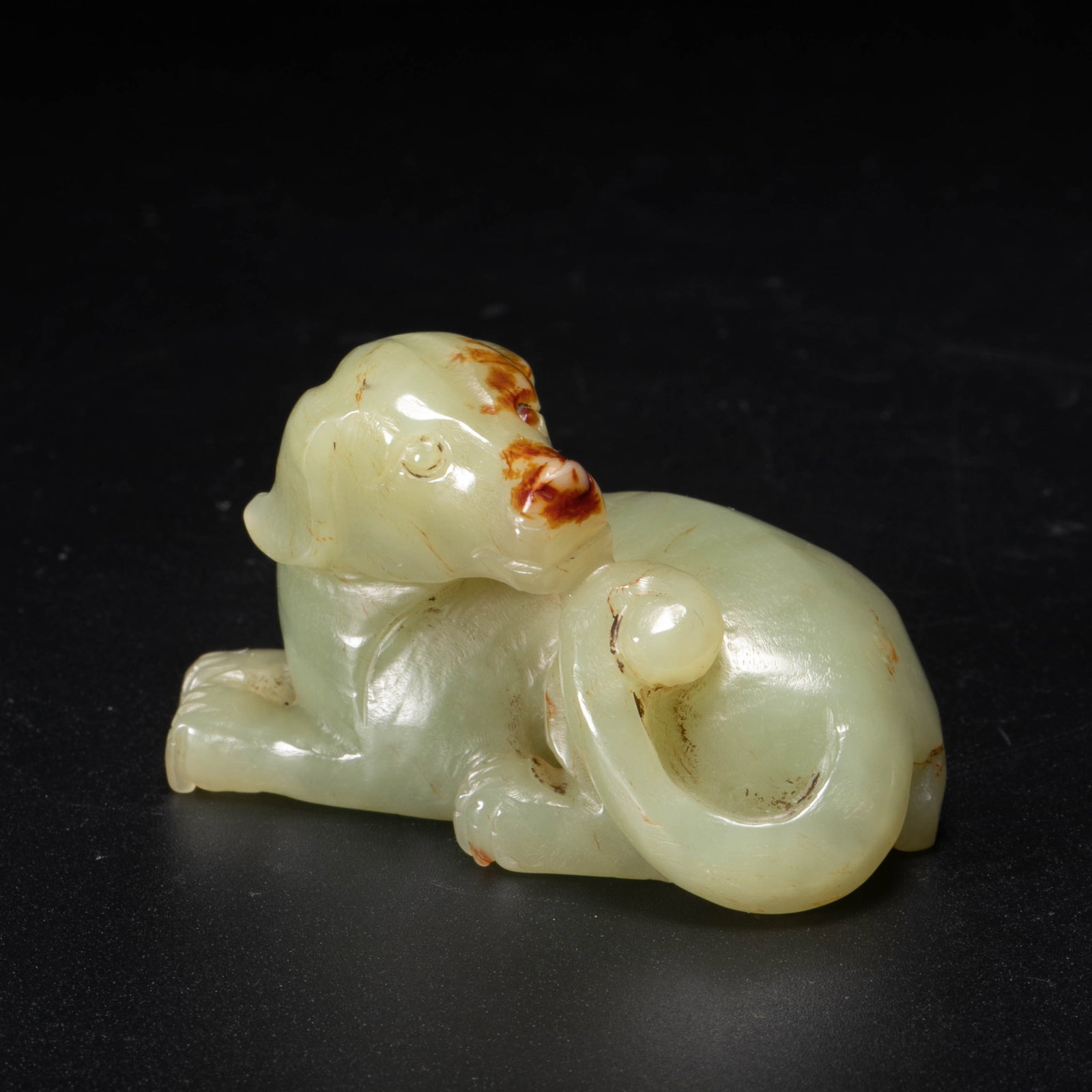 Republic of China jadeite dog with russet skin, looking back: This small topaz looking back dog ornament from the Republic of China is made of green topaz, which is warm and slightly translucent. It has a brownish-red skin color in parts, like autumn maple