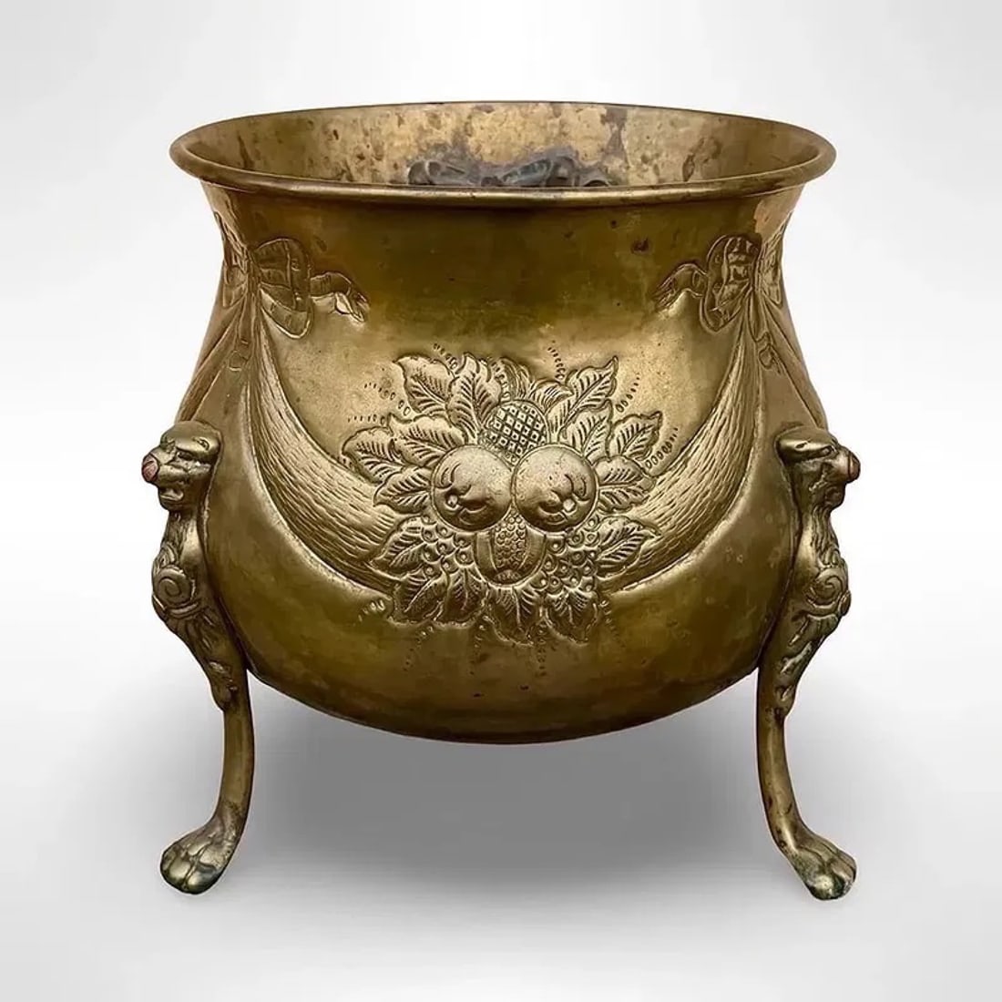 Repoussé Brass Floral Jardinière: Antique floral repoussé brass jardinière with lion paw feet. Decoated with raised fruit-and-foliage motifs and ribbon-tied swags. Approx. Dimensions: 8W × 8D × 8H inches