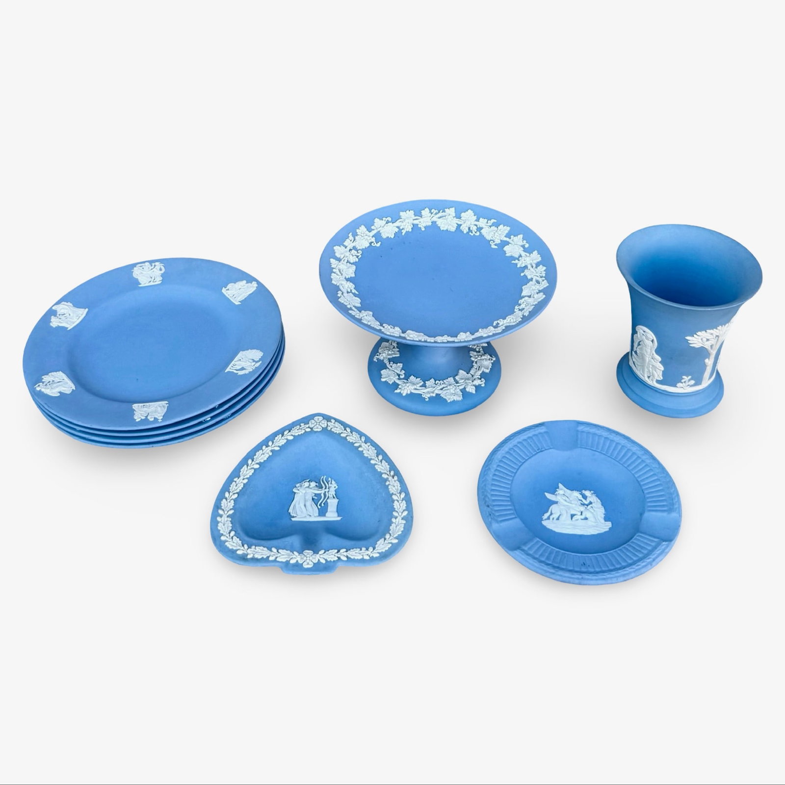 8 Pc Wedgwood Blue Jasperware Set: Wedgwood Blue Jasperware collection with white neoclassical relief decoration. Includes four dessert plates, a pedestal cake stand, a vase or cup, a heart-shaped dish, and a small circular dish. Appro