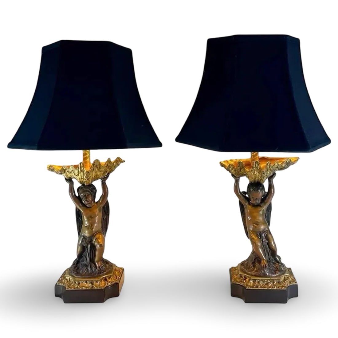 French Bronze Putti Lamps, Pair: French Bronze Putti Lamps, Pair Pair of antique gilt and patinated bronze Leviton corded table lamps with cherub figures supporting large shells on a black stone base. Each lamp is fitted with a navy 