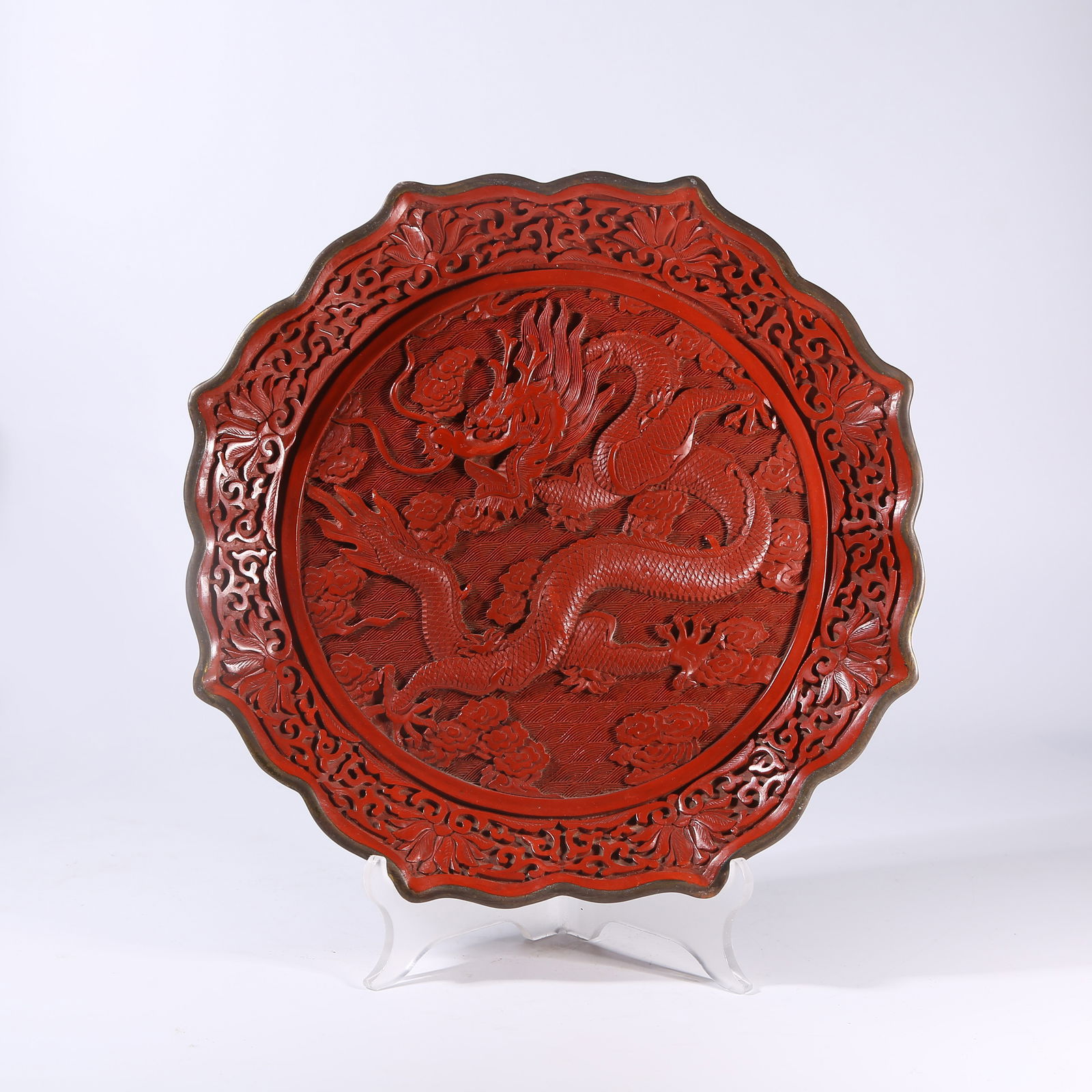 A CARVED RED LACQUER PLATE WITH CLOUD AND DRAGON MOTIF AND FLOWER RIM: Carved Red Lacquer Plate with Cloud and Dragon Motif and Flower Rim