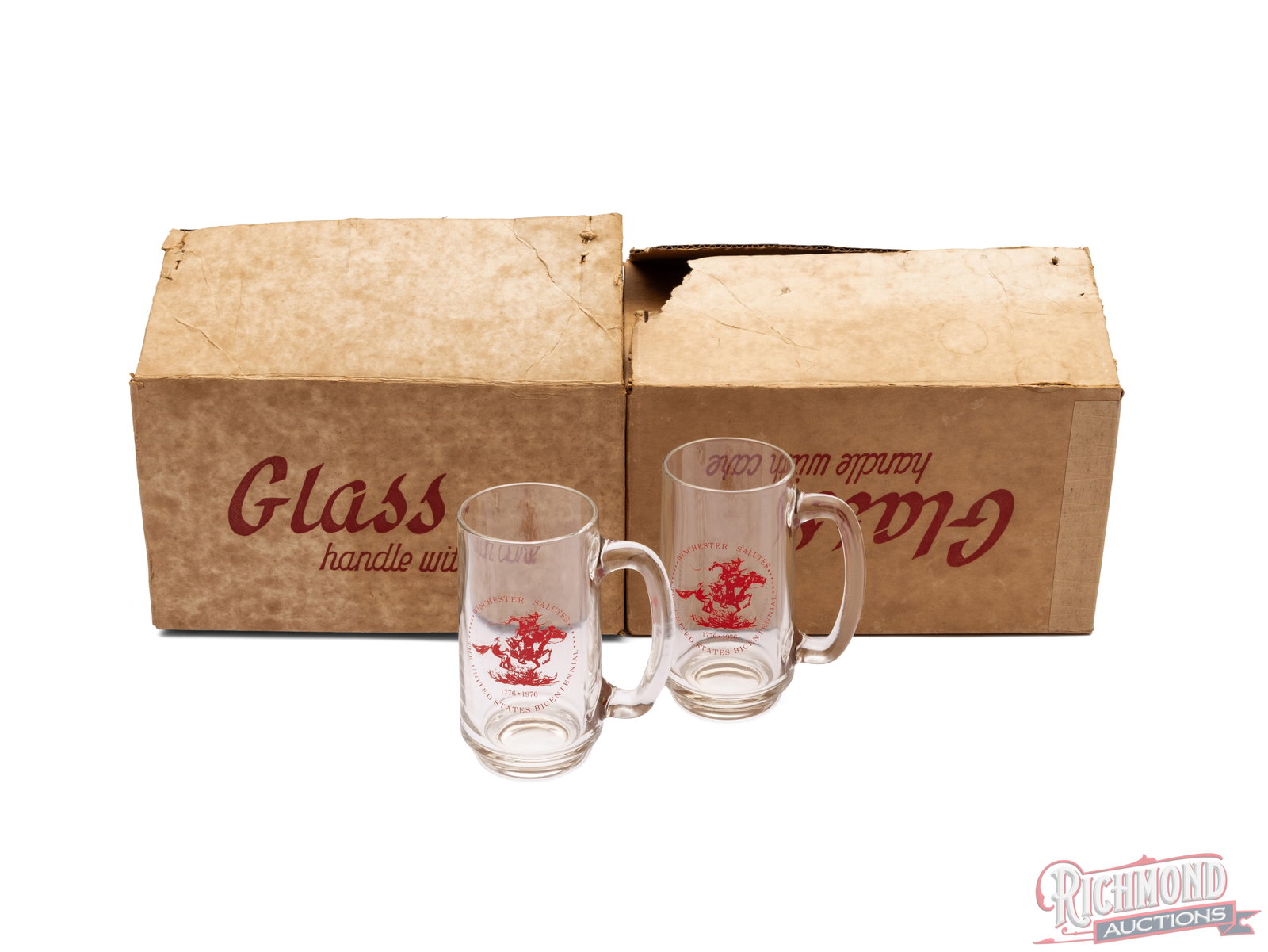 Set of Eight Winchester US Bicentennial Glass Mugs: In this lot is two cases, each with four glasses, of Winchester glass mugs commemorating the United States bicentennial. The mugs feature the Winchester horse and rider logo with "1776-1976" below.
