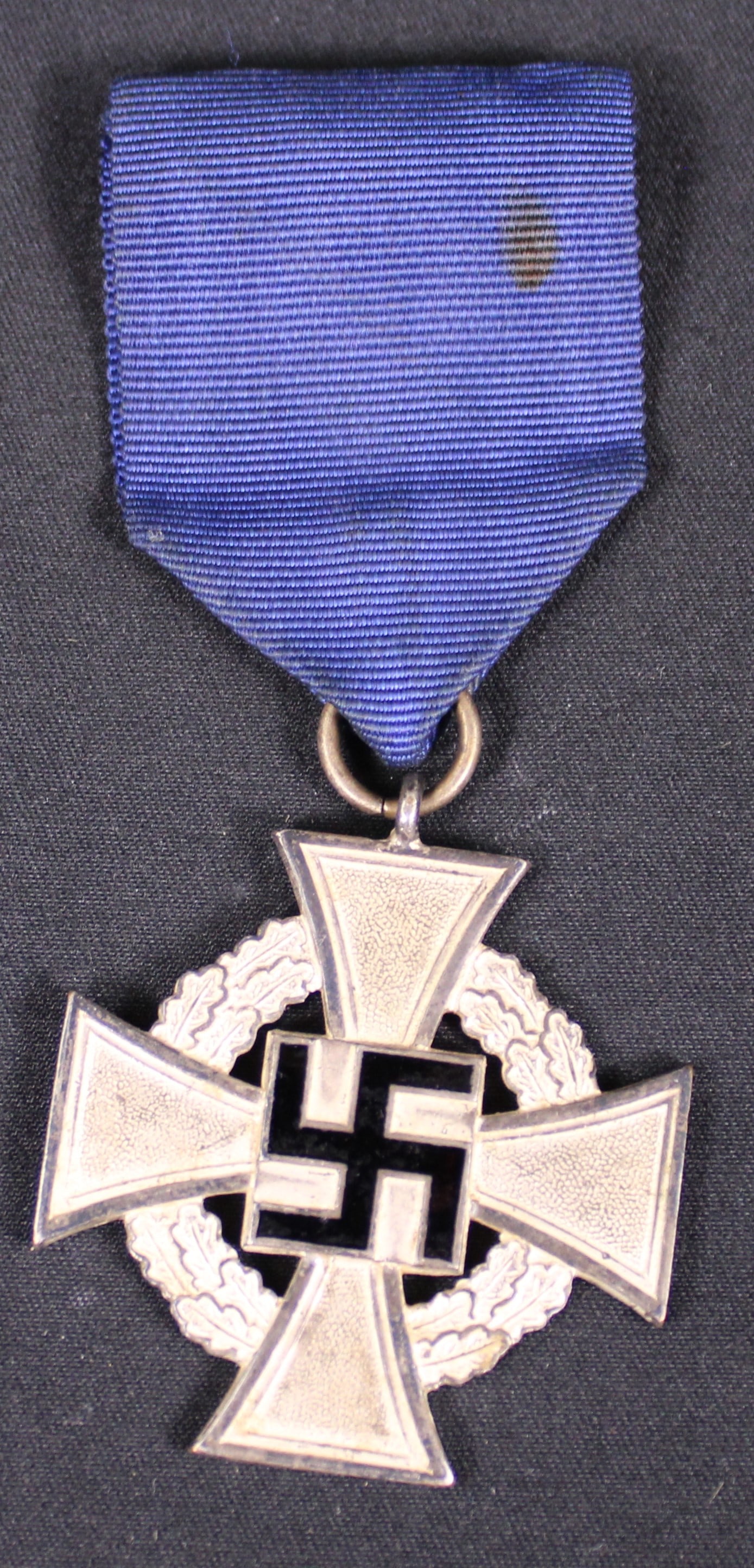 German WWII 25-Year Civil Service Faithful Service Medal (BTJ): This German WWII 25-Year Civil Service Faithful Service Medal features a silver cross with a black enamel swastika and an oak leaf wreath, attached to a blue ribbon. Overall this item seems to be in