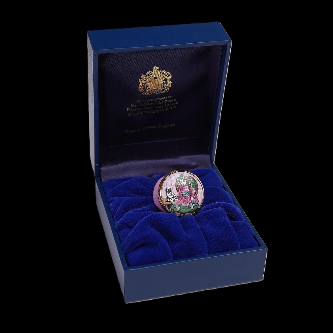 Halcyon Days Doll & Dog Enamel Box: Enchanting miniature pink enamel decorative box featuring a charming depiction of a doll in a pink dress accompanied by a small black–and–white dog, set against a detailed background. The 