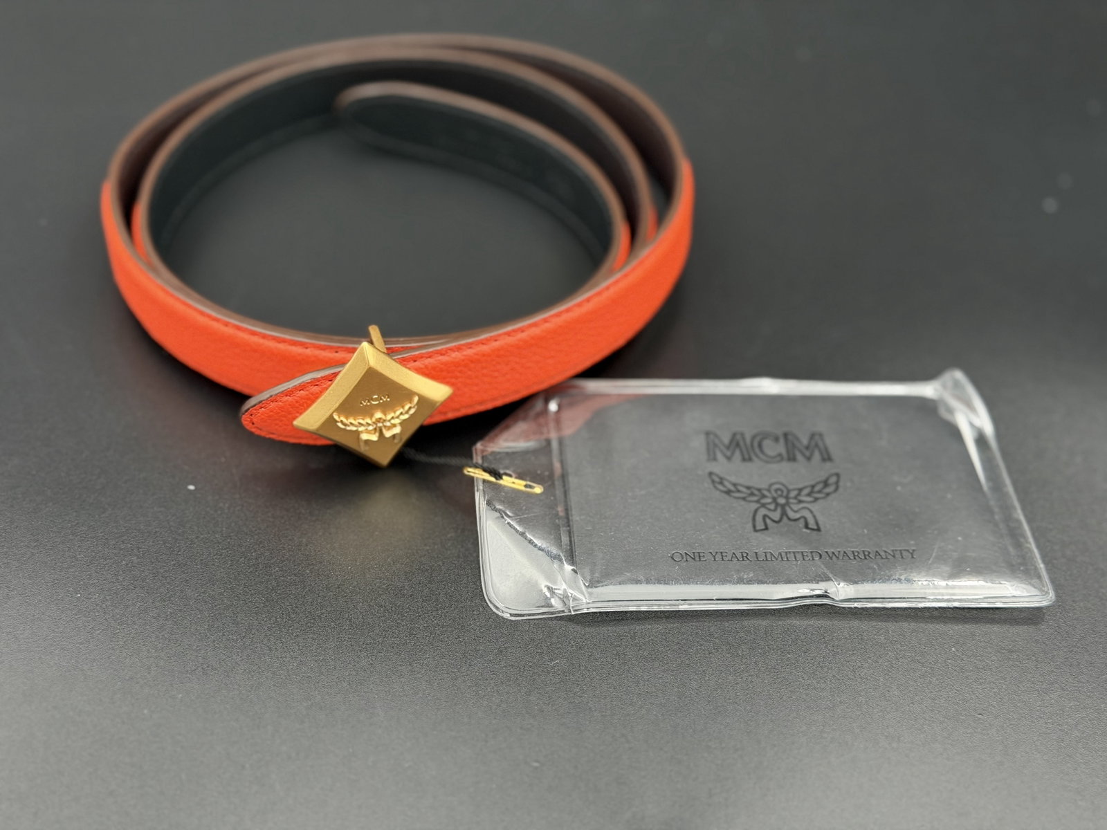 MSRP $390 MCM Orange Diamond Buckle Leather Belt NWT: MCM leather belt featuring vibrant orange leather construction and the brand’s signature diamond-shaped gold-tone buckle with raised MCM logo motif. Slim-profile accessory accompanied by origina