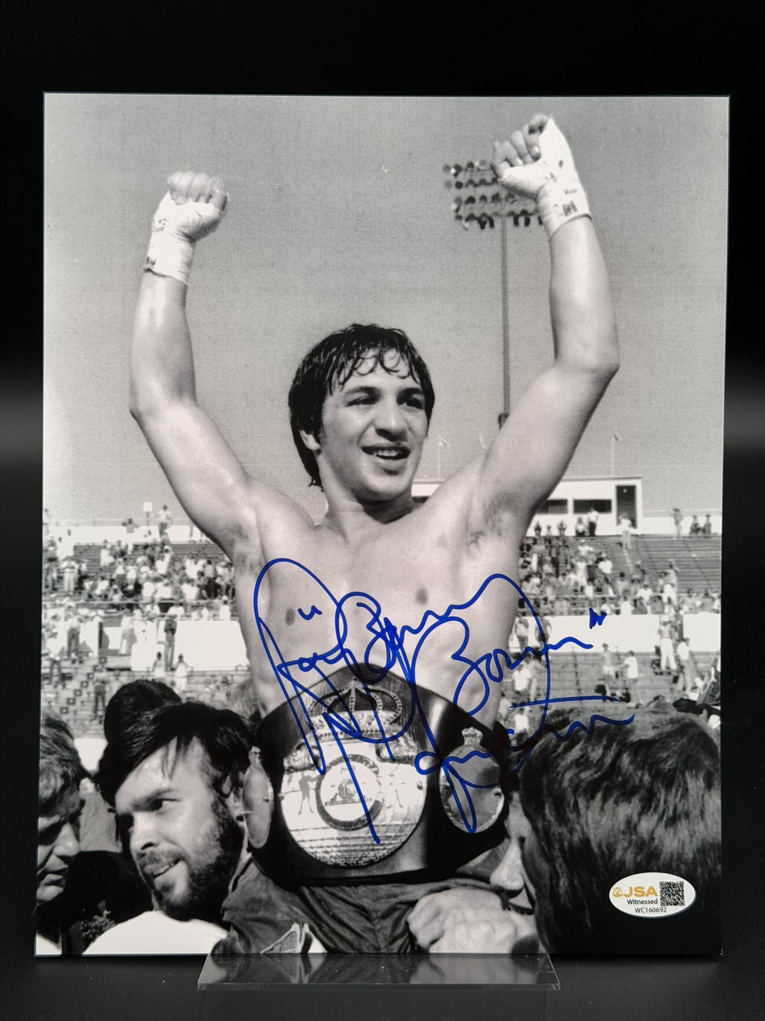 Ray Boom Boom Mancini Signed Boxing Champion Celebration Photo JSA COA 8" × 10": Black-and-white photograph personally signed by legendary boxing champion Ray "Boom Boom" Mancini in bold blue marker across the front. The iconic image captures Mancini celebrating with his champions