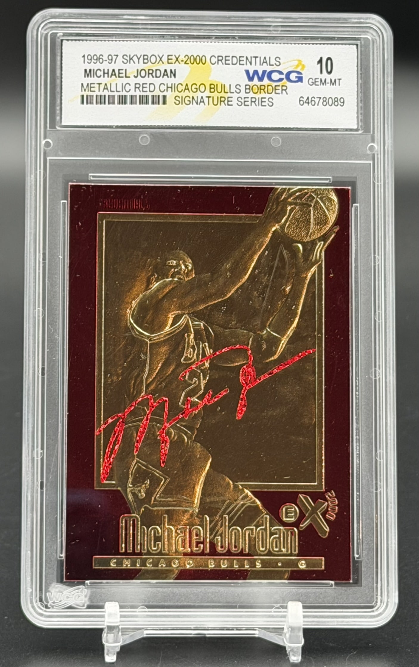 1996-97 SkyBox E-X2000 Credentials Michael Jordan Metallic Red Border WCG 10 Signature Series: 1996-97 SkyBox E-X2000 Credentials Michael Jordan Signature Series card with metallic red border, professionally graded WCG Gem-MT 10. The front of this premium metallic collectible features a gold-sc