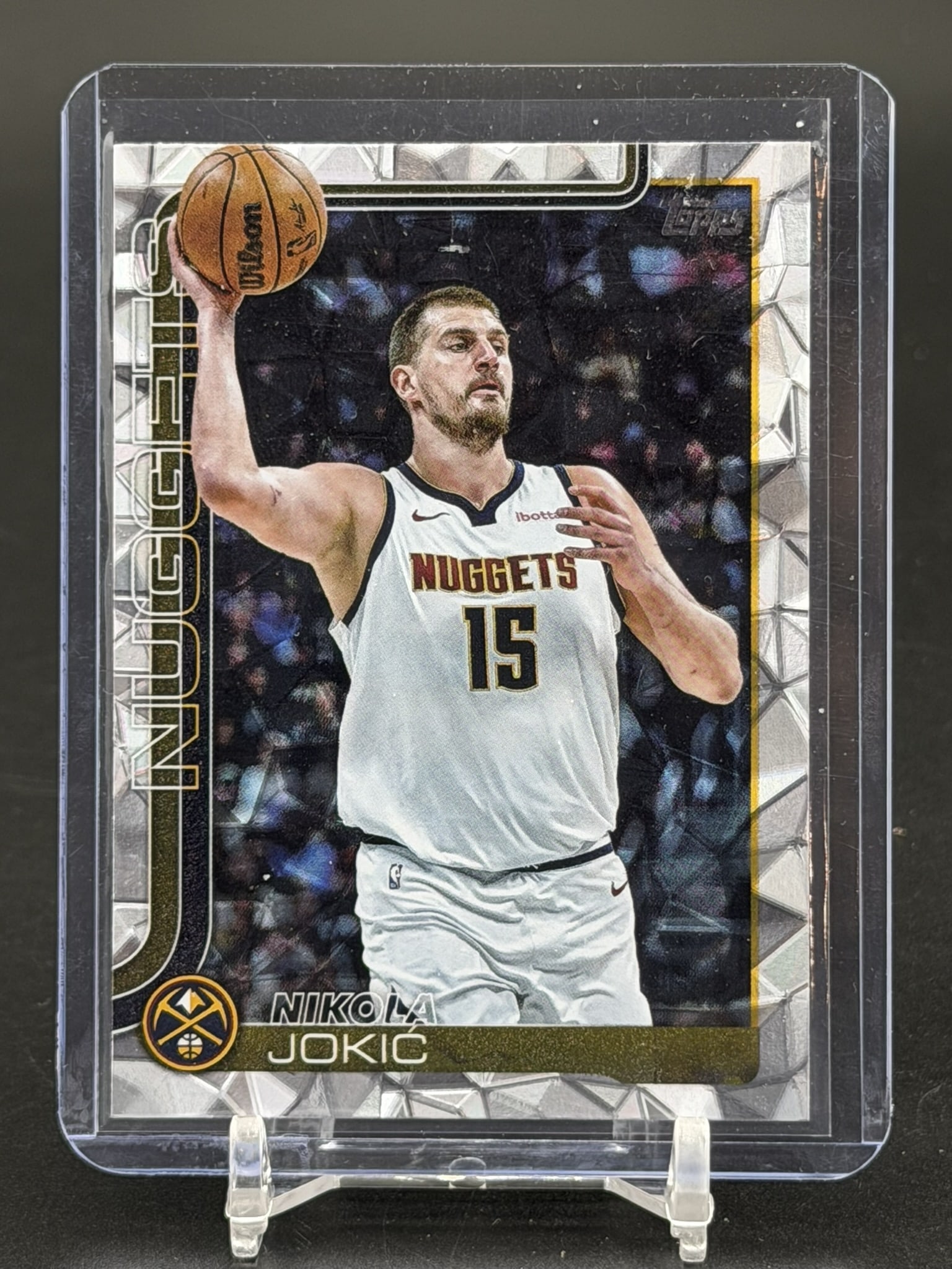 2025 Topps Nikola Jokić Silver Foil Prizm Card #101 Denver Nuggets Center Basketball: 2025 Topps Nikola Jokić card #101 featuring the Denver Nuggets center. The front of this card showcases an action photograph of Jokić holding a basketball in his white Nuggets uniform, s