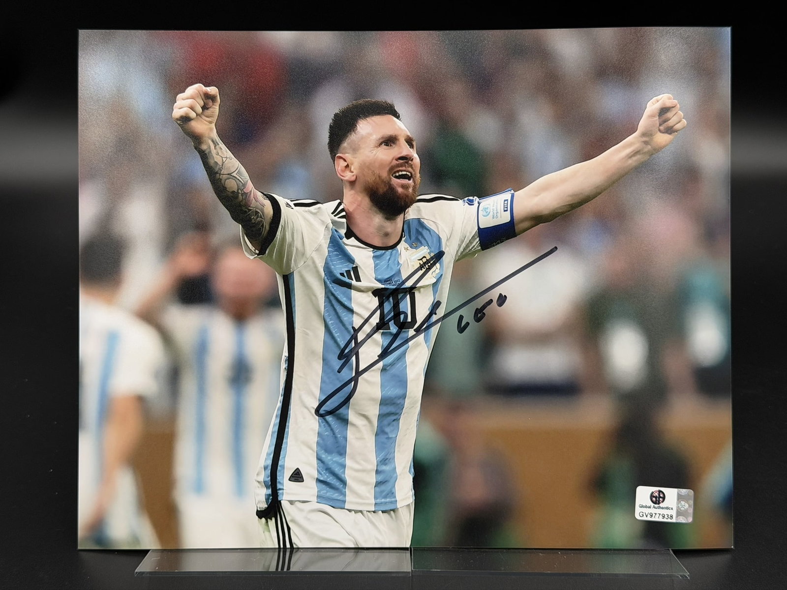 Lionel Messi Signed Argentina Photo GA COA 8" × 10": Color photograph personally signed by Lionel Messi in silver marker, depicting the legendary Argentine footballer celebrating while wearing the Argentina national team jersey. The piece measures appro