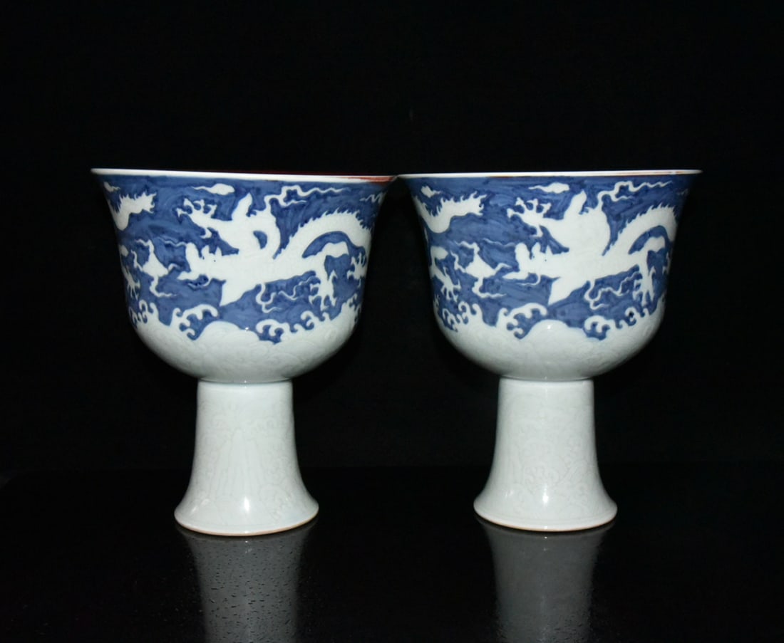 A pair of Ming Dynasty Xuande period blue-and-white stemmed bowls with incised dragon design and a: pair of Ming Dynasty Xuande period blue-and-white underglaze blue high-footed bowls with incised dragon design and a red glaze, measuring 21 x 18.5 cm. Provenance:From a private collection in Sussex,