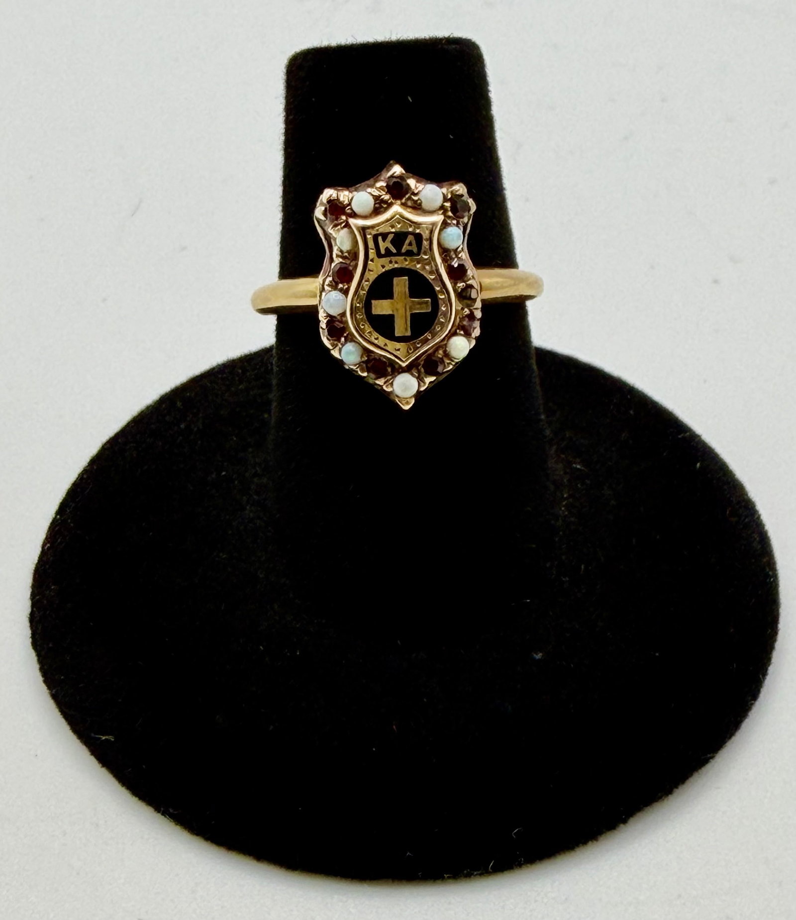 Vintage Kappa Alpha Theta Sorority Ring: A gold-toned Kappa Alpha Theta sorority ring featuring ‘KA’ and a cross in gold against a black enameled shield. The shield is further embellished with facet cut garnets and round opals. T
