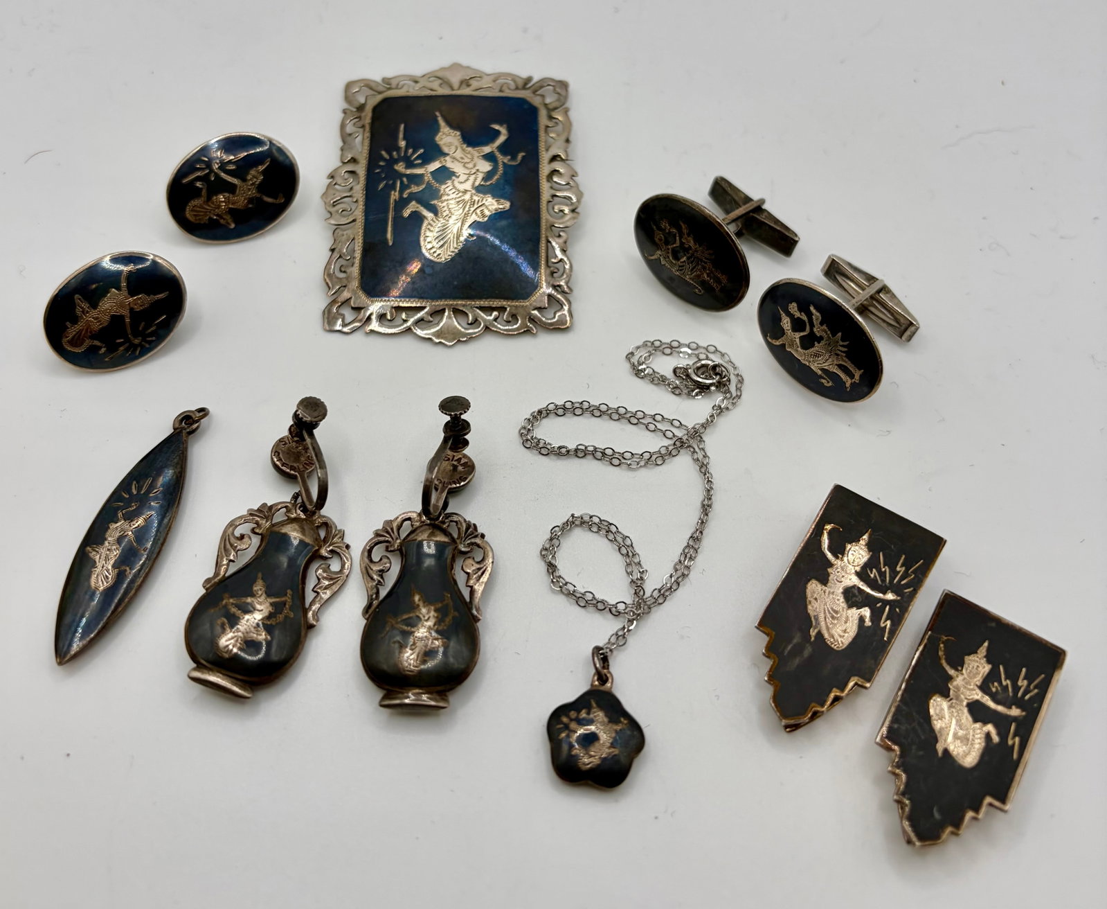 Collection of Vintage Sterling Silver & Niello Jewelry Marked Siam: A collection of vintage sterling silver and niello jewelry. The collection includes a brooch, a pair of shoe clips, two pairs of screw-back earrings, a pair of cufflinks, two pendants & an 18” c