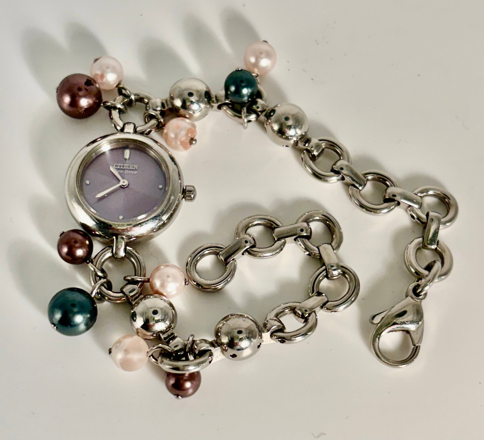 Women’s Citizen Eco-Drive Watch: A Citizen Eco-Drive women’s watch featuring a faux pearl beaded bracelet. The watch face has an iridescent pink dial with silver-tone hands and markers. The Eco-drive technology means it is powe