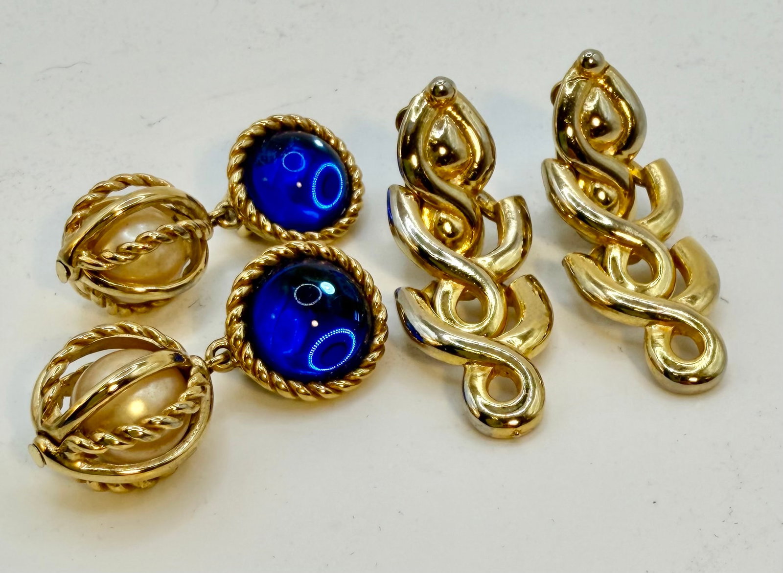 Pairs of Givenchy and Paolo Crucci Clip Earrings: Two vintage pairs of designer gold-toned clip earrings. The Paolo Crucci earrings have two hinged elements that hang from the clip. They are 2” long and 0.75” wide. The Givenchy pair featu