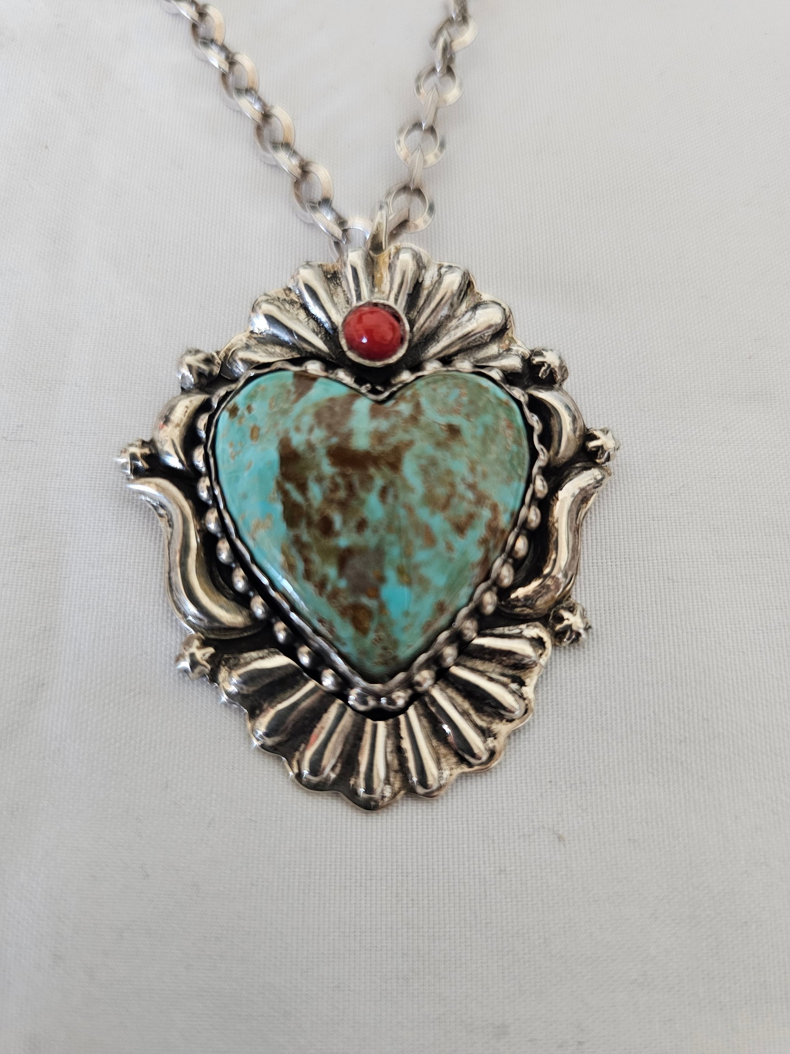 Tony Chino Sterling Silver Turquoise Heart Pendant Necklace 36.26g: Signed sterling silver turquoise heart pendant by Tony Chino, featuring a large heart-shaped turquoise cabochon with warm brown matrix, accented by a small red coral cabochon and surrounded by substan