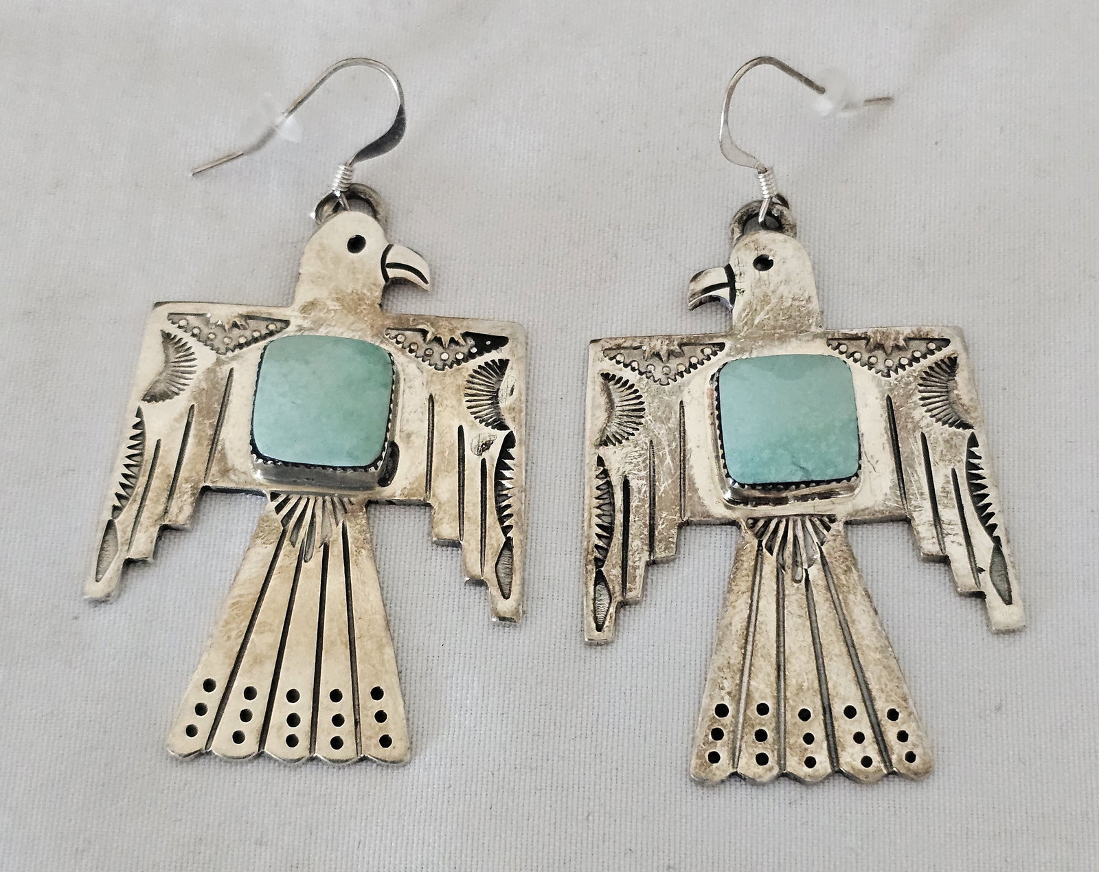 J. Delgarito Navajo Sterling Silver Thunderbird Earrings with Blue-Green Stone: Large sterling silver thunderbird dangle earrings by Navajo silversmith J. Delgarito. Each stylized thunderbird is hand stamped and set with a square blue-green cabochon at the center. Signed J. Delga