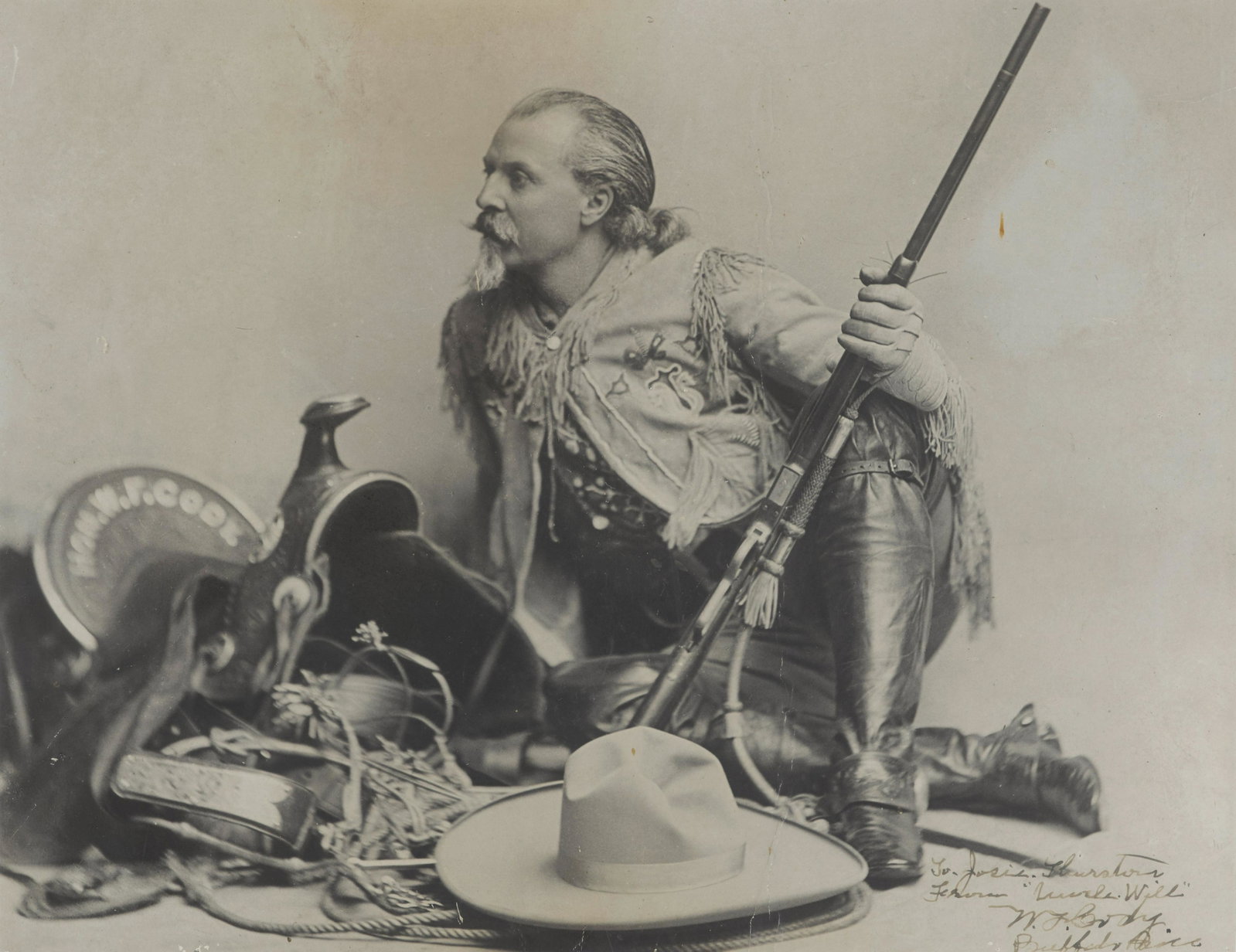 CODY, WILLIAM F. 'BUFFALO BILL.' 1846-1917.: CODY, WILLIAM F. 'BUFFALO BILL.' 1846-1917. Photograph Signed and Inscribed (''Uncle Will' / W.F. Cody'), mammoth gelatin silver print portrait of Cody with saddle, hat and gun, 10 1/2 x 13 1/2 inches