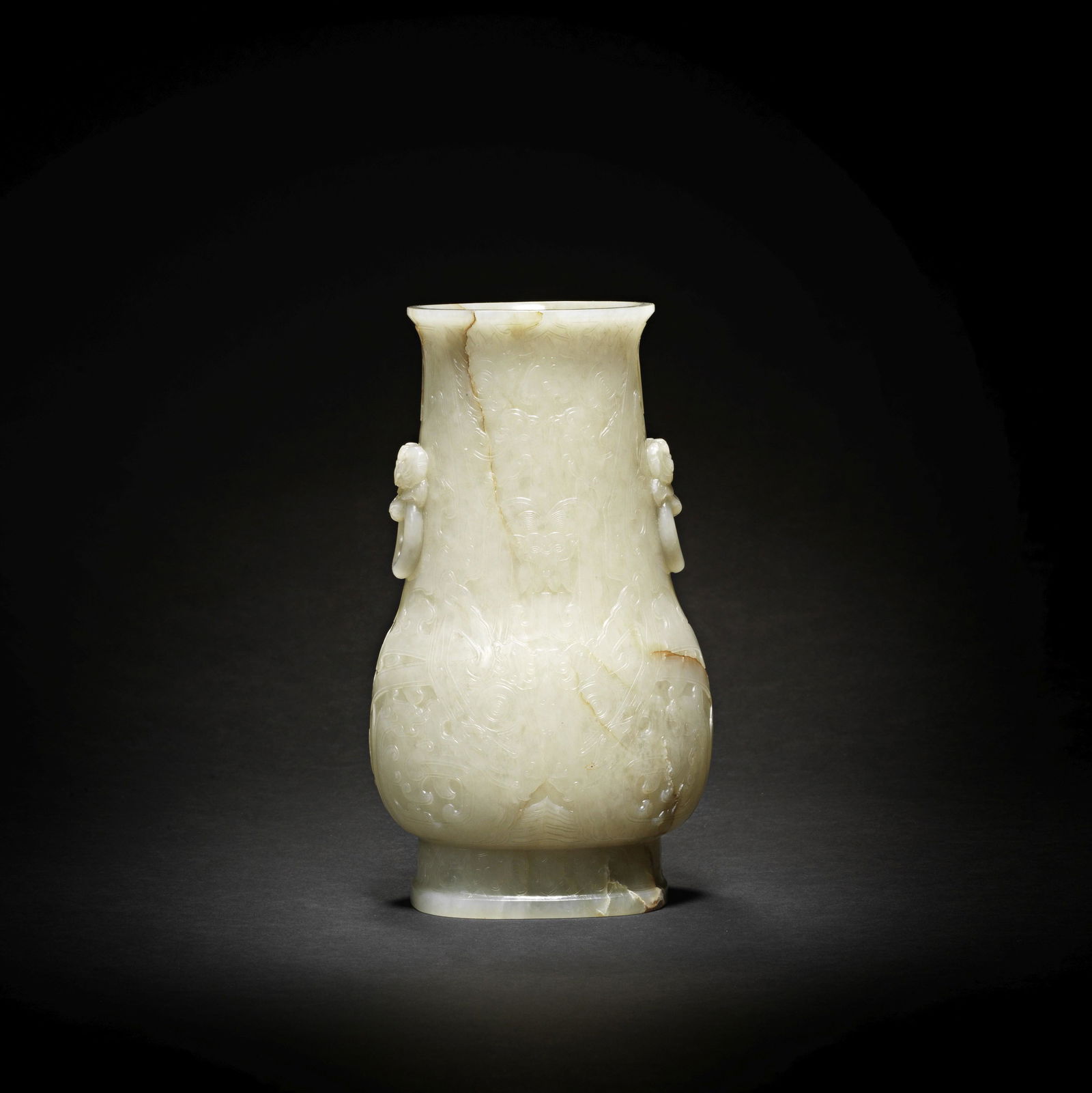 A VERY RARE AND LARGE PALE WHITE GREEN AND BROWN-STREAKED JADE VASE, HU Ming Dynasty: A VERY RARE AND LARGE PALE WHITE GREEN AND BROWN-STREAKED JADE VASE, HU Ming Dynasty The vase of flattened pear shape rising from a spreading stepped foot to an everted rim, the body intricately carve