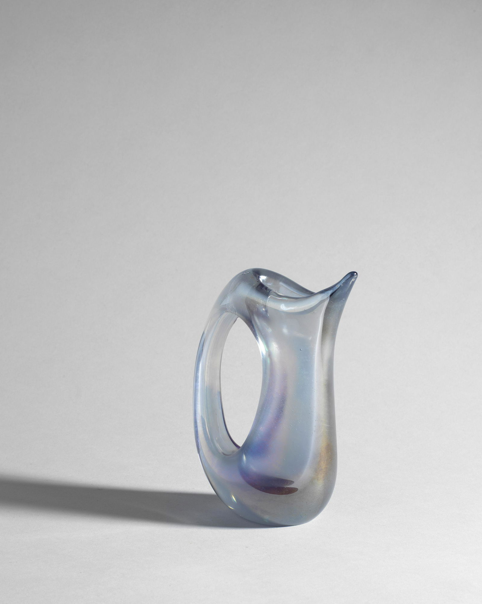 Giorgio Ferro Pitcher, from the 'Anse Volanti' series, circa 1952: Giorgio Ferro Pitcher, from the 'Anse Volanti' series, circa 1952 Iridescent coloured glass. 17 x 12.5 x 6.6cm Produced by A.V.E.M., Murano, Italy. Footnotes: Literature 'Murano alla Biennale', Domu