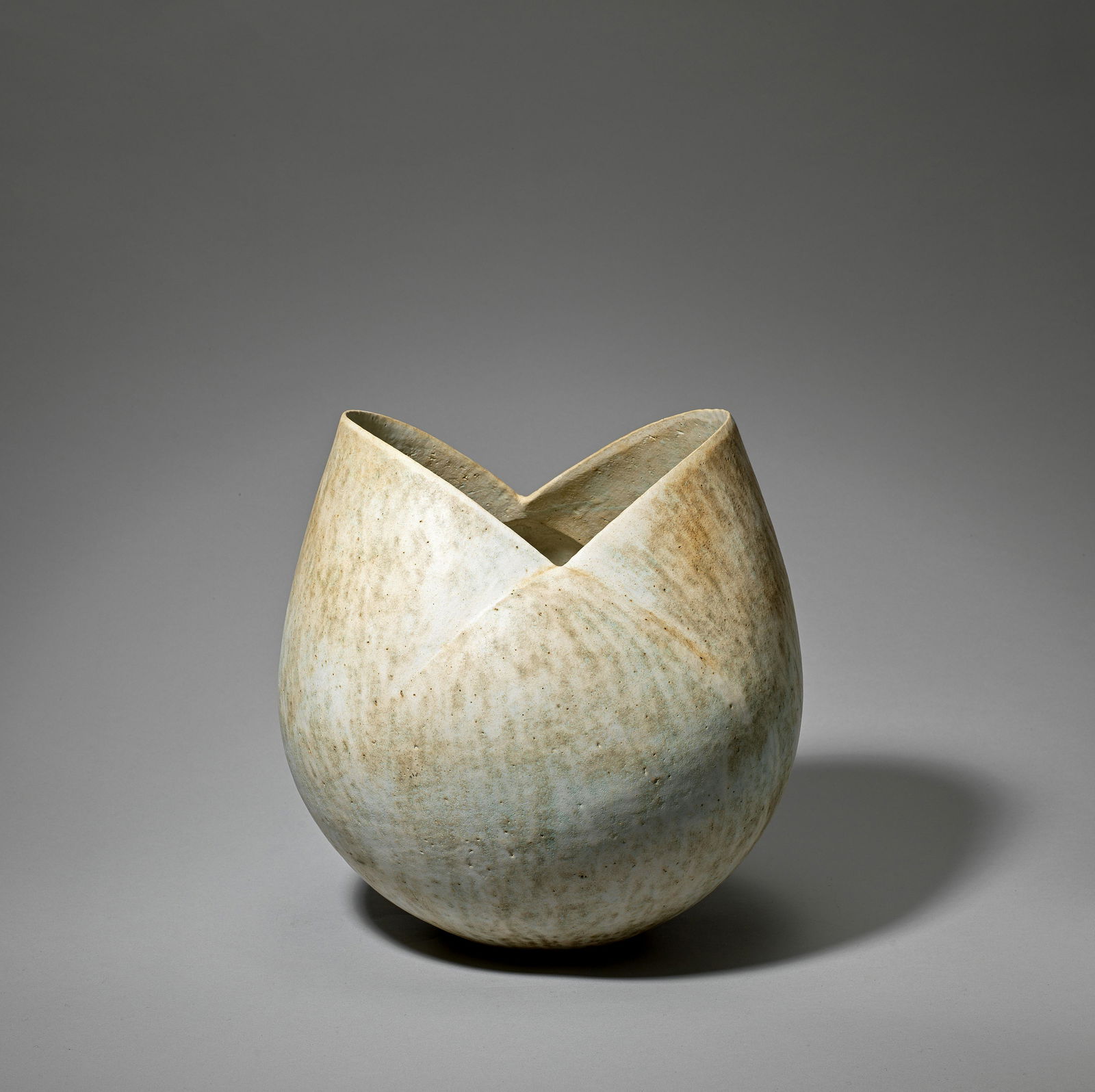John Ward 'Bud pot', circa 1985: John Ward'Bud pot', circa 1985Stoneware, the diagonally cut neck rim with extending impressed grooves to the shoulder, mottled cream, green and brown matt glazes over a softly textured surface.32 cm h