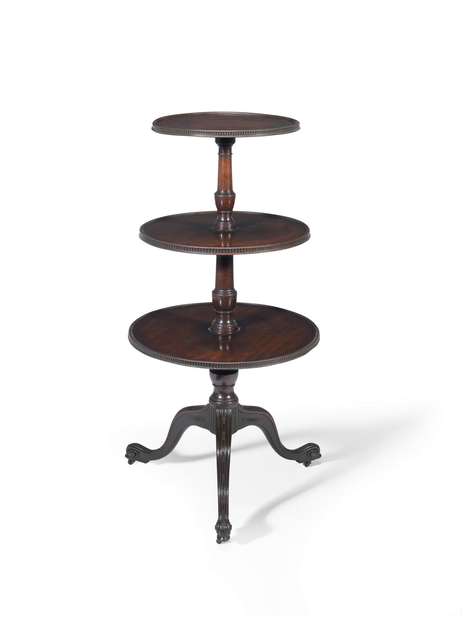 A George III mahogany three-tier dumb waiterIn the manner of Thomas Chippendale: A George III mahogany three-tier dumb waiter In the manner of Thomas Chippendale The graduated and revolving tiers with fluted and beaded mouldings, the vase shaped turned columns on a bead moulded tr