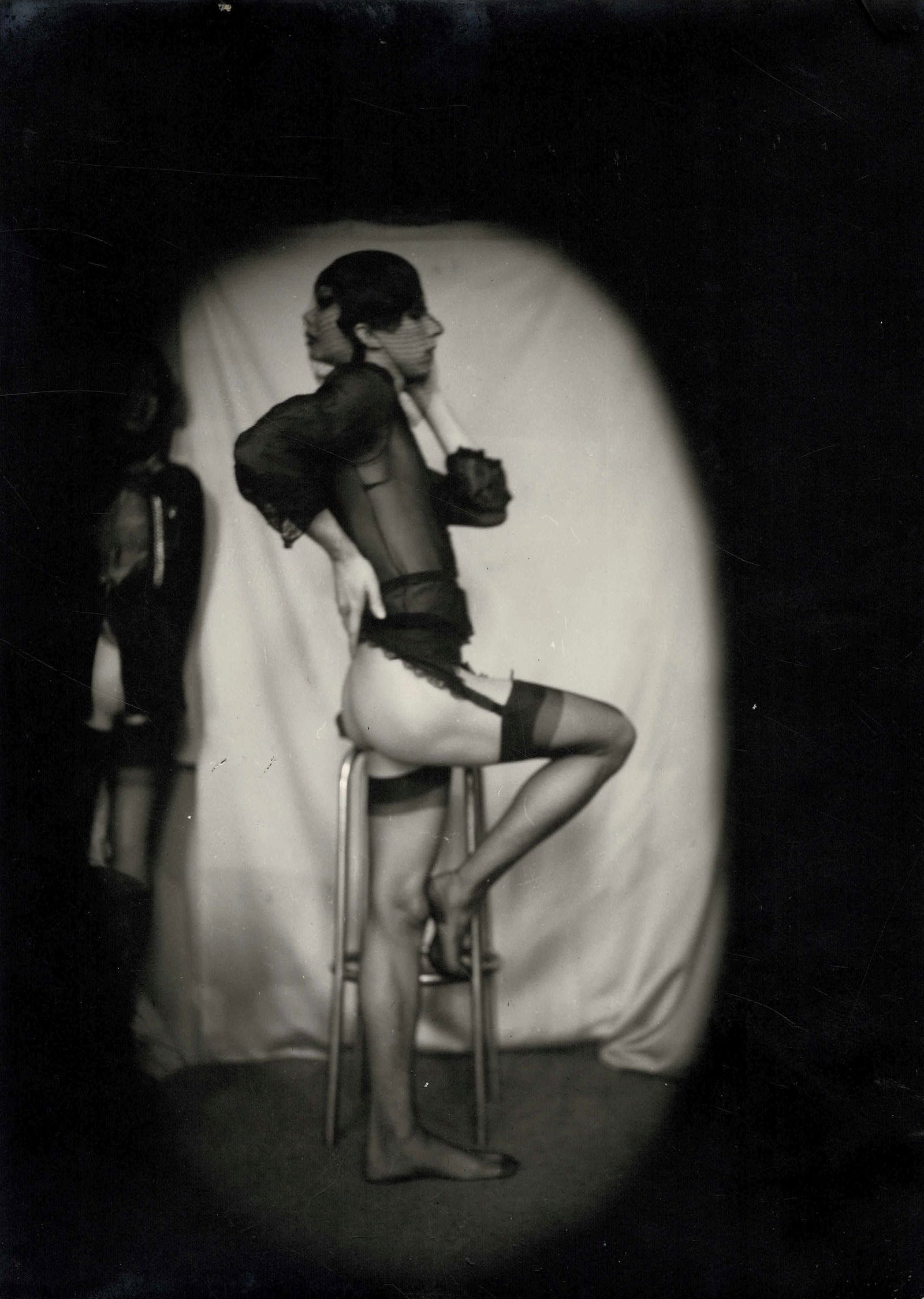 Pierre Molinier (1900-1976) Luciano Castelli avec le masque à l'occiput, sur le tabouret, 1...: Pierre Molinier (1900-1976) Luciano Castelli avec le masque à l'occiput, sur le tabouret, 1975. Tirage argentique d'époque sur papier Agfa. Gelatin silver print on Agfa paper. 17,7 x 12,5 cm