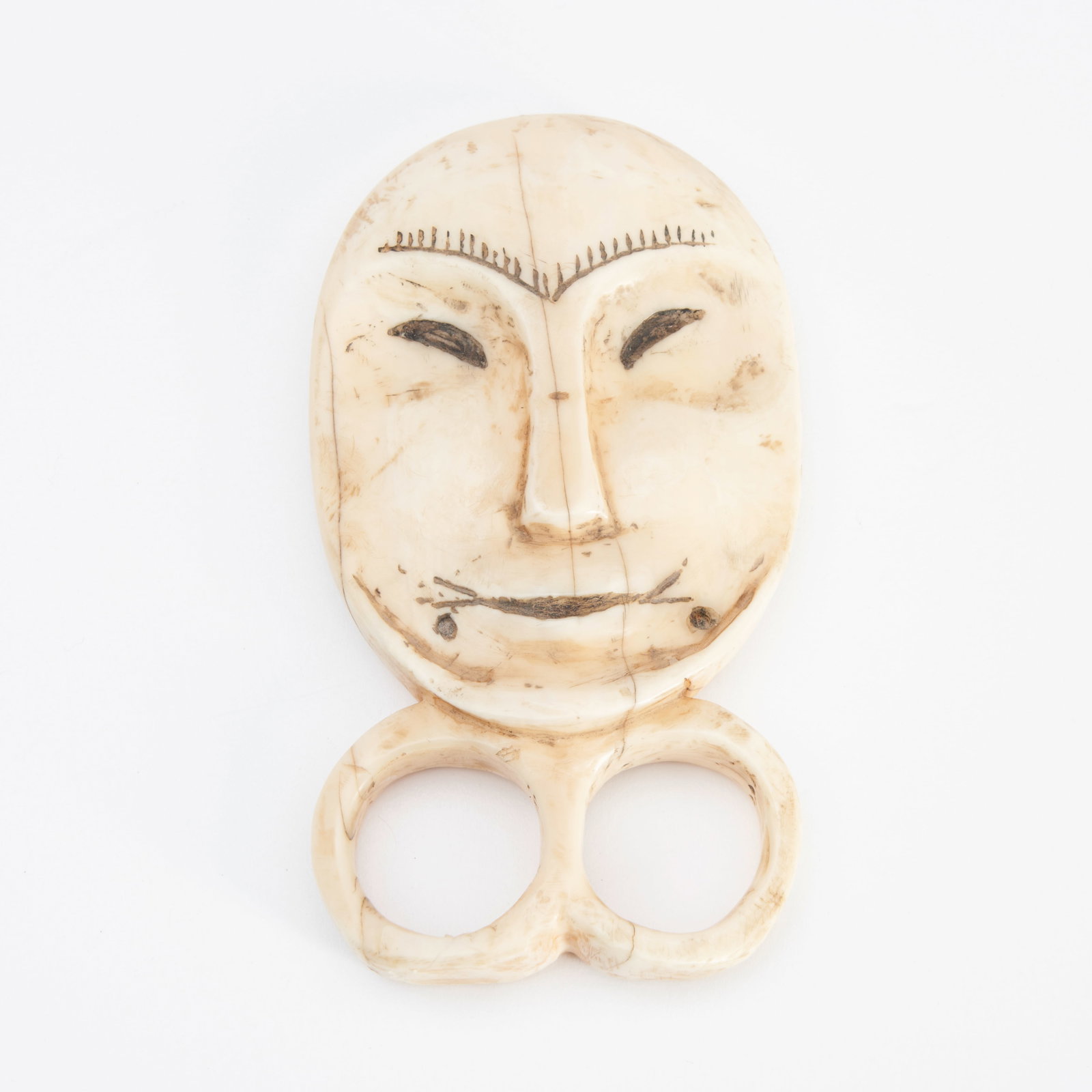 An Eskimo finger mask lg. 3 7/8 in.: An Eskimo finger mask Of typical form, carved from walrus tusk and depicting a man's face, the incised features enhanced with dark pigment. lg. 3 7/8 in. Footnotes: Provenance: Galerie Elca, London, M