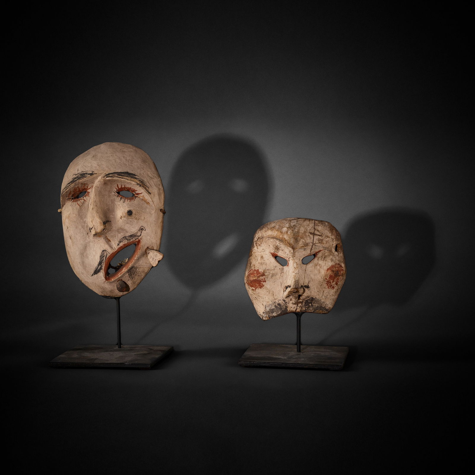 Two Inuit masks: Two Inuit masks Each of carved and polychrome painted wood with pierced eyes, the first with a crooked nose and applied side labrets, the second a half-mask example ending at the upper lip, the second